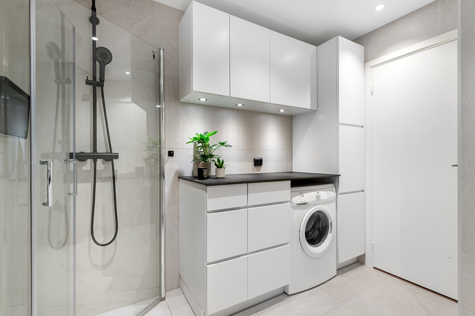 Dusjhjørne med dører og vegghengt dusjarmatur med hånddusj og regndusj. Gulvstående toalett. Opplegg for vaskemaskin Galleribilde