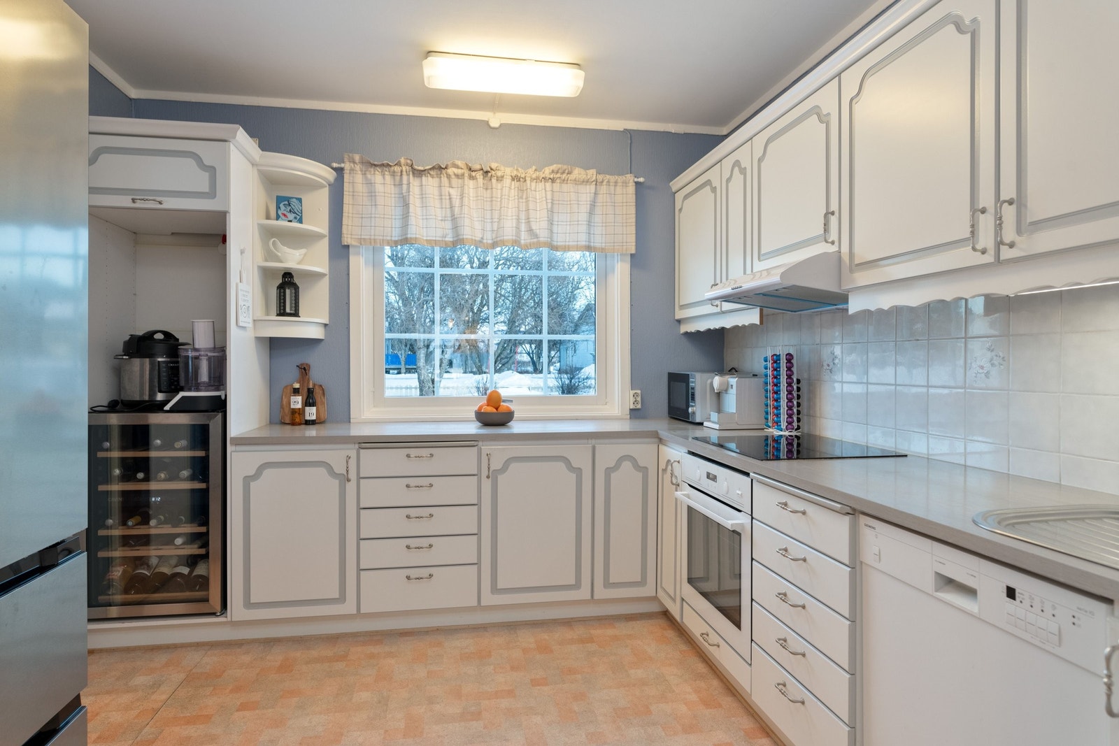 Kjøkken med utsikt mot hagen. Kjøkkenløsning inkluderer vinskap, stor side-by-side kjøleskap, induksjonsovn og moderne oppvaskmaskin Galleribilde