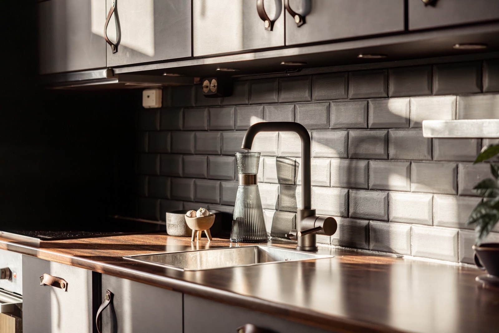 Sorte glatte fronter på kjøkken, med grep i skinn og malte fliser på vegg. Galleribilde