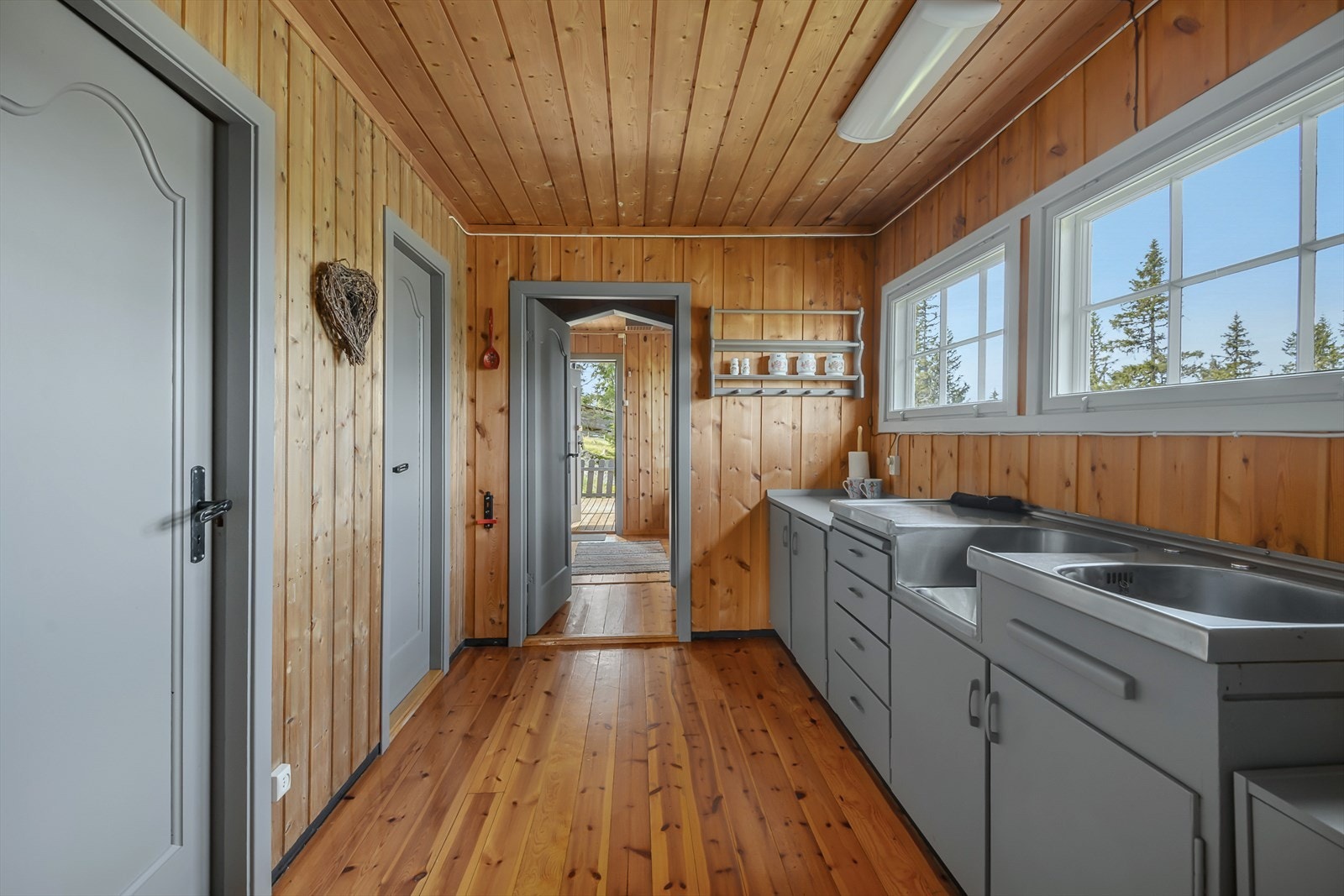 Eldre kjøkkeninnredning som er malt i en delikat gråtone. Fint lys inn over kjøkkenbenken. Galleribilde