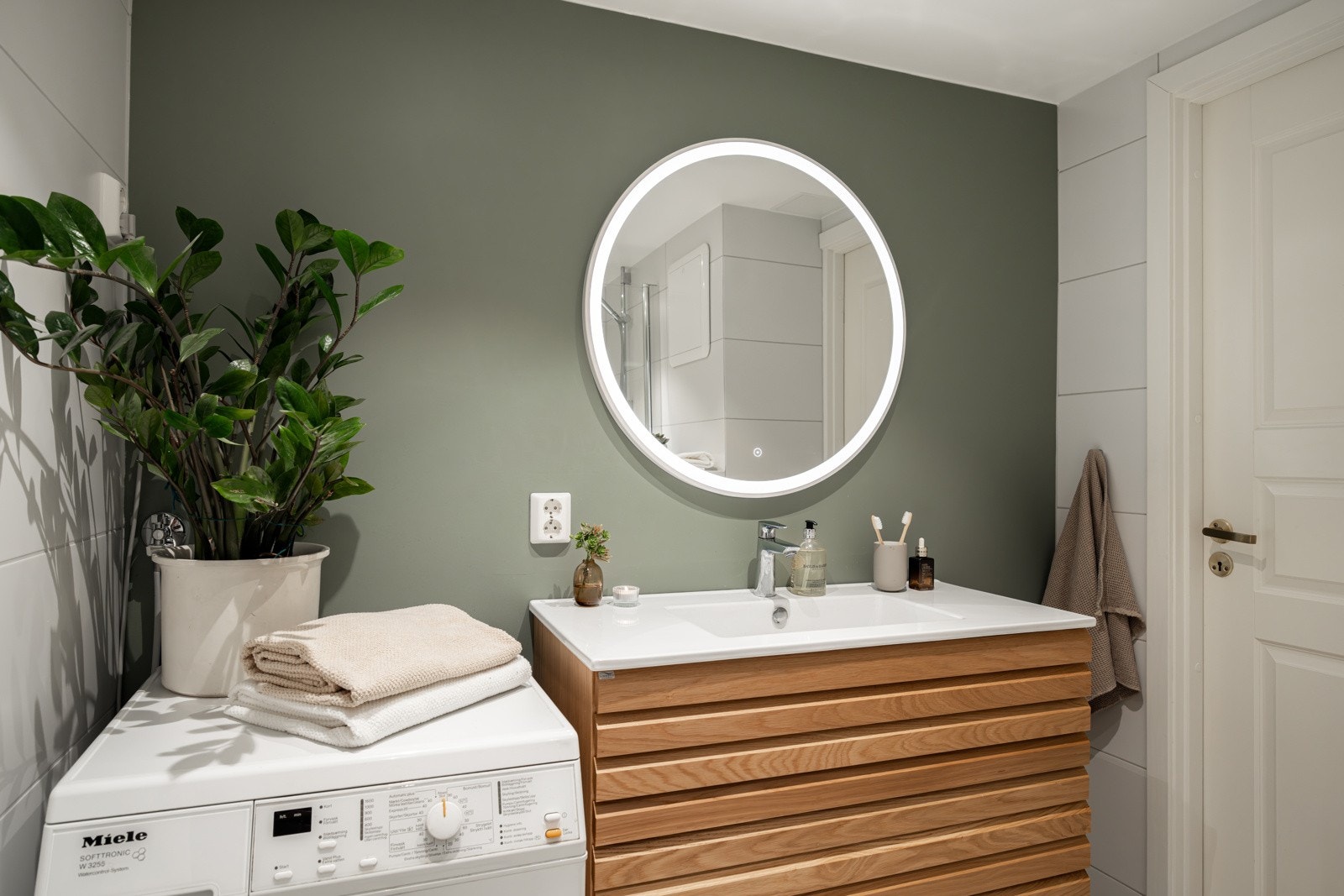 Vegghengt servantinnredning med profilerte fronter, heldekkende servant med ett-greps armatur og speil over servant med integrert lys. Galleribilde