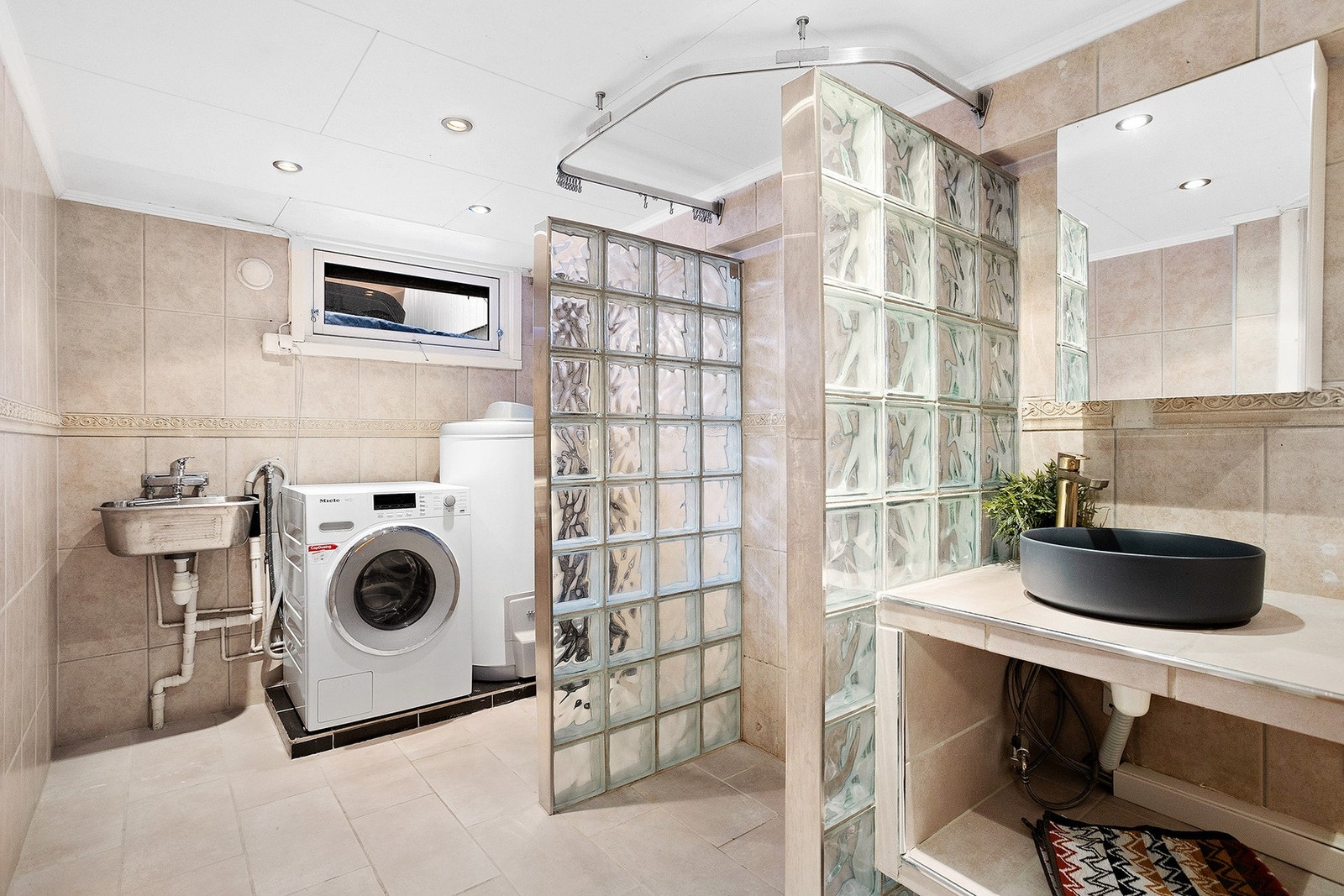 Underetasjen byr på et stort og praktisk bad/vaskerom. Her finner du en dusjnisje med glassbyggerstein og forheng, vegghengt toalett, hylle med bolleservant og speil, samt utslagsvask. Galleribilde