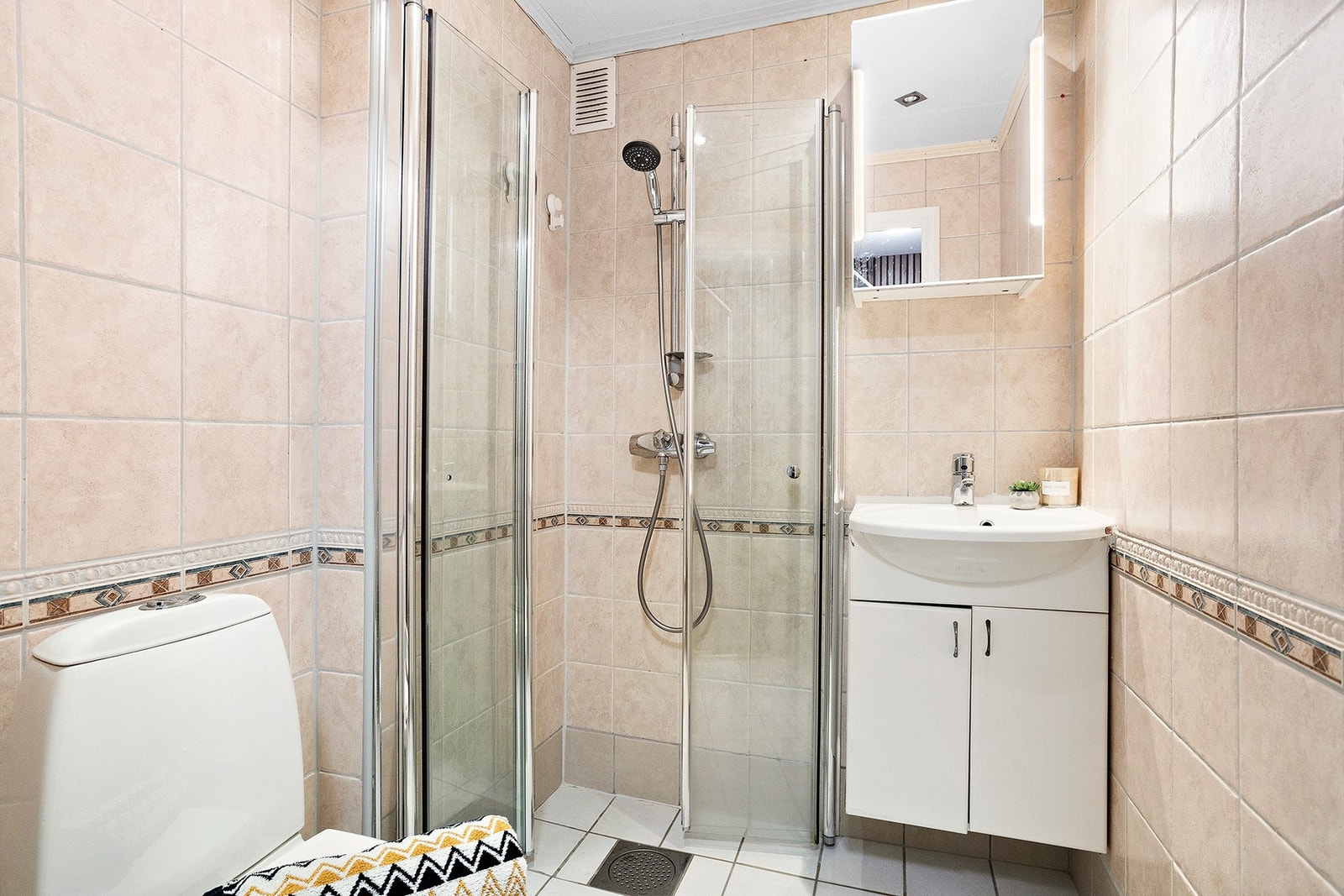 Badet er innredet med dusjhjørne med glassvegger, gulvmontert toalett og en innredning med nedsunket servant og speil. Galleribilde