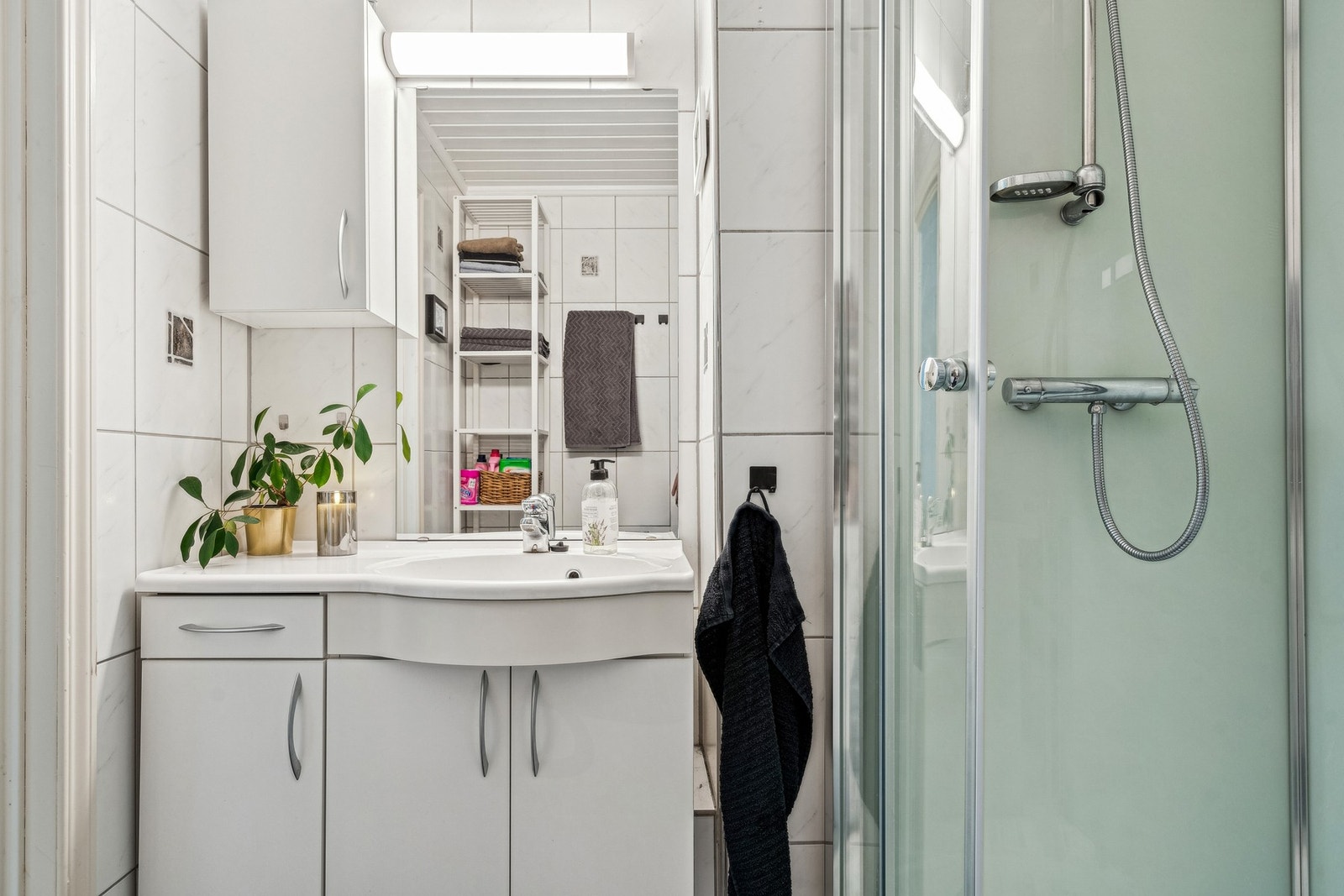 Badet har hvit servantinnredning med lys over speilet, dusjkabinett, gulvmontert toalett og opplegg for vaskemaskin. Galleribilde