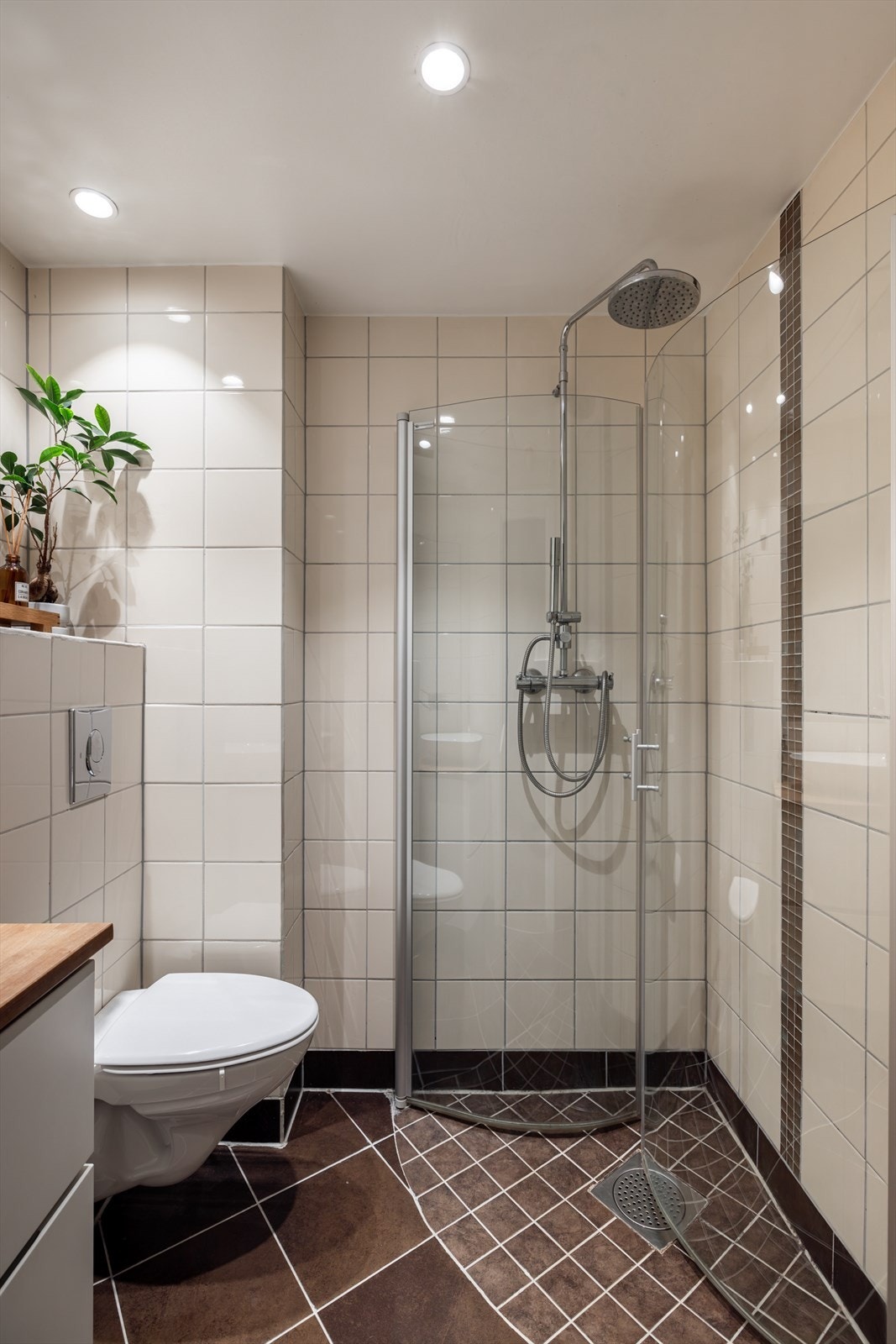 Badet er innredet med vegghengt klosett, en servant på møbel med heltre benkeplate, speil og et dusjhjørne med svingbare glassdører. Galleribilde