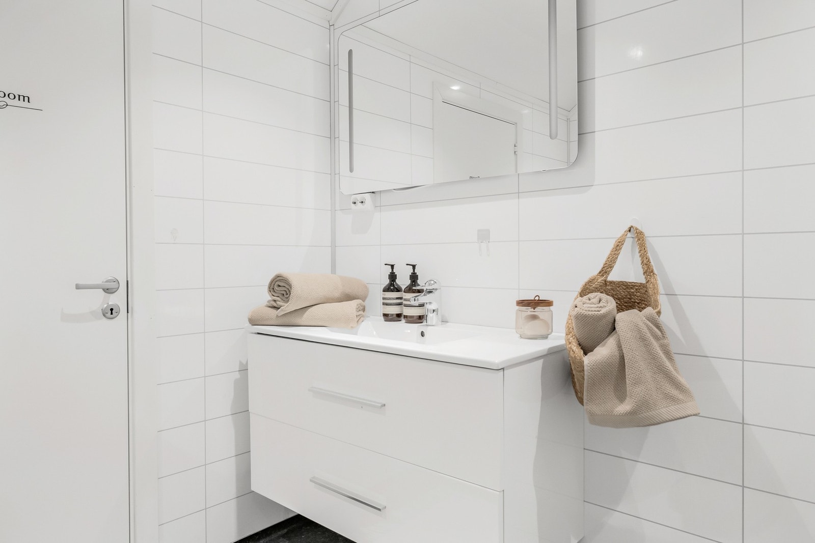 Badet er innredet med baderomsinnredning i hvit høyglans med heldekkende servant, veggmontert toalett og dusjkabinett Galleribilde