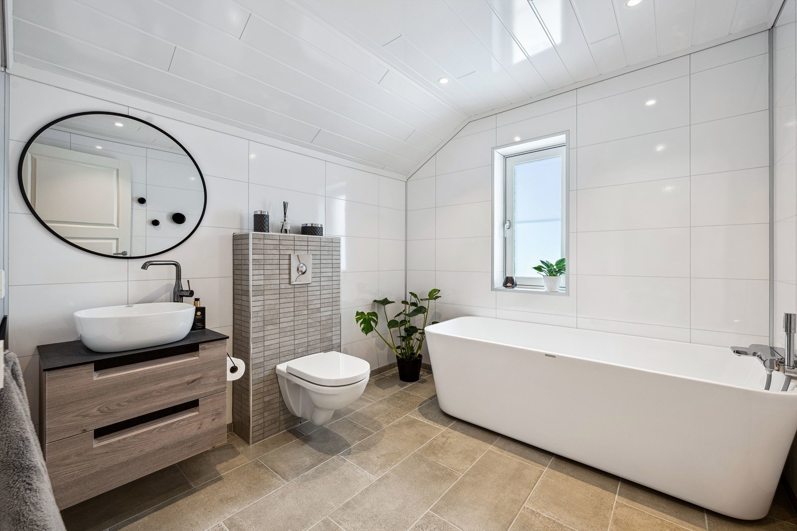 Stilfullt bad med vegghengt wc, badekar og praktisk innredning med vask. Flislagt gulv med varmekabler. Galleribilde