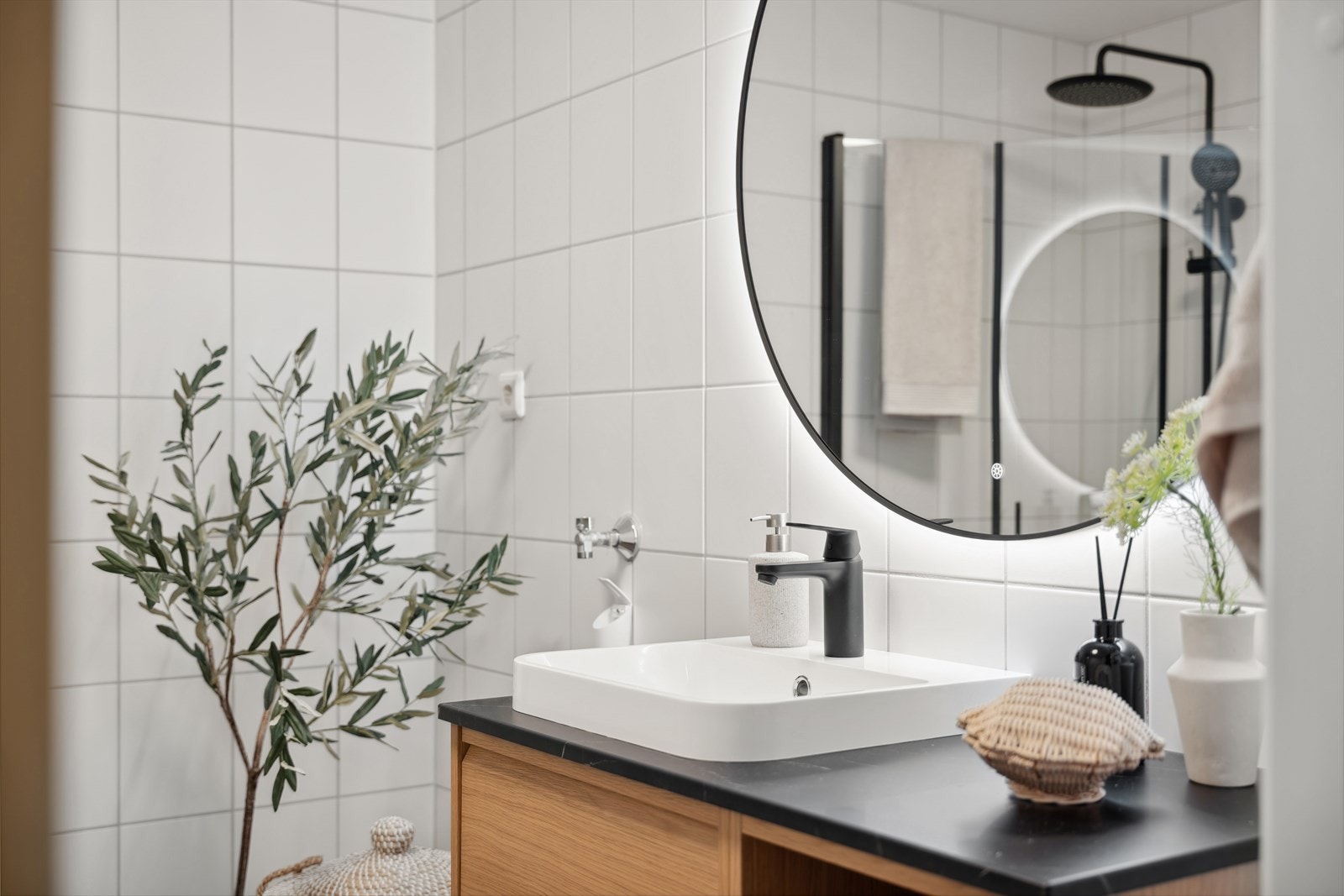 Badet er utstyrt med en finert servantinnredning med praktiske skuffer og hyller, et dusjhjørne med sorte, elegante glassdører og regndusj for en spa-lignende opplevelse. Galleribilde