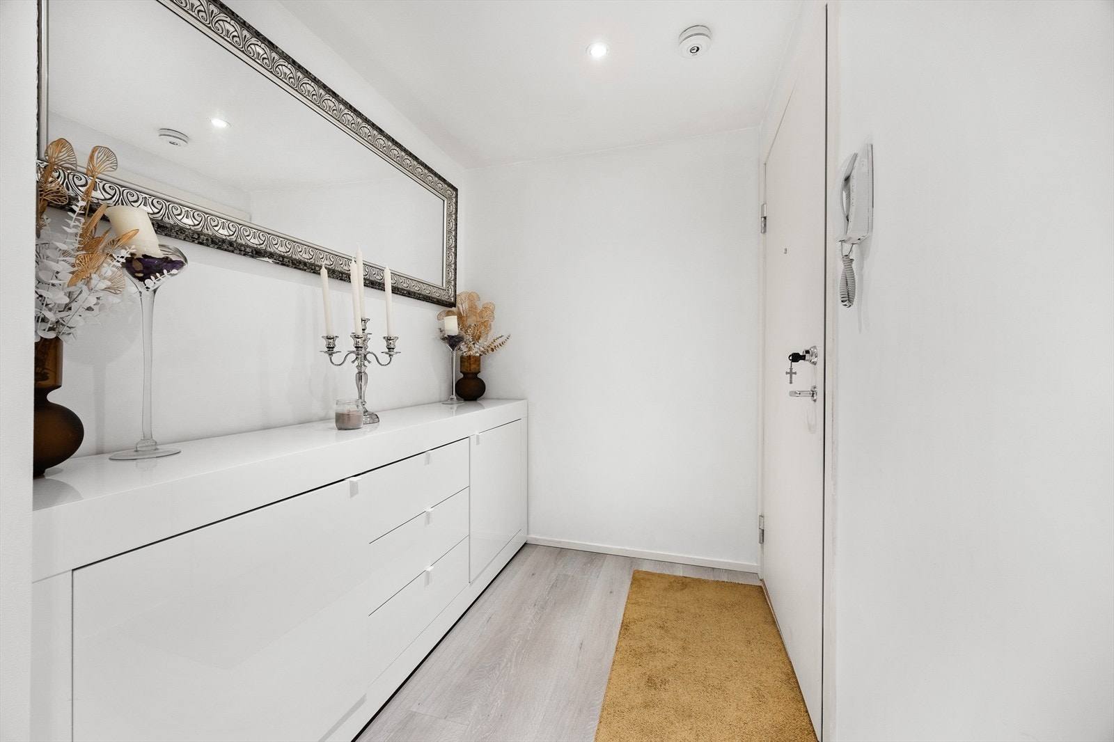 En innbydende entré/gang som er med på å gi et godt førstegangsinntrykk av resten av leiligheten. Gulvet er belagt med en lys og moderne laminat, på vegger er det lysmalte plater malt i en dus farge, og i himling er det hvitmalte plater med downlights. Galleribilde