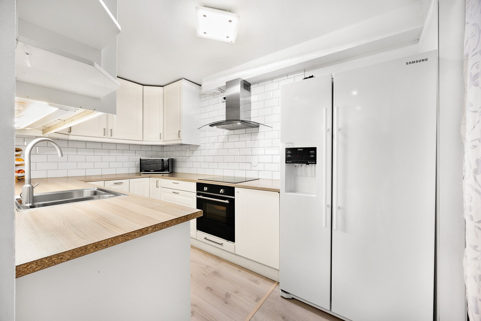 Kjøkkeninnredningen består av lyse profilerte fronter i både over- og underskap, belysning under overskap, laminat benkeplate med dobbel oppvaskkum, og integrerte hvitevarer som oppvaskmaskin, stekeovn, og platetopp. Galleribilde