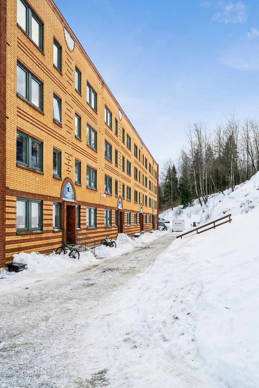 Leiligheten ligger med endebeliggenhet i boligblokkens oppgang A. Utenfor inngangspartiet er det tilrettelagt lekeplass for barna og grillplass med sittebenker. Galleribilde