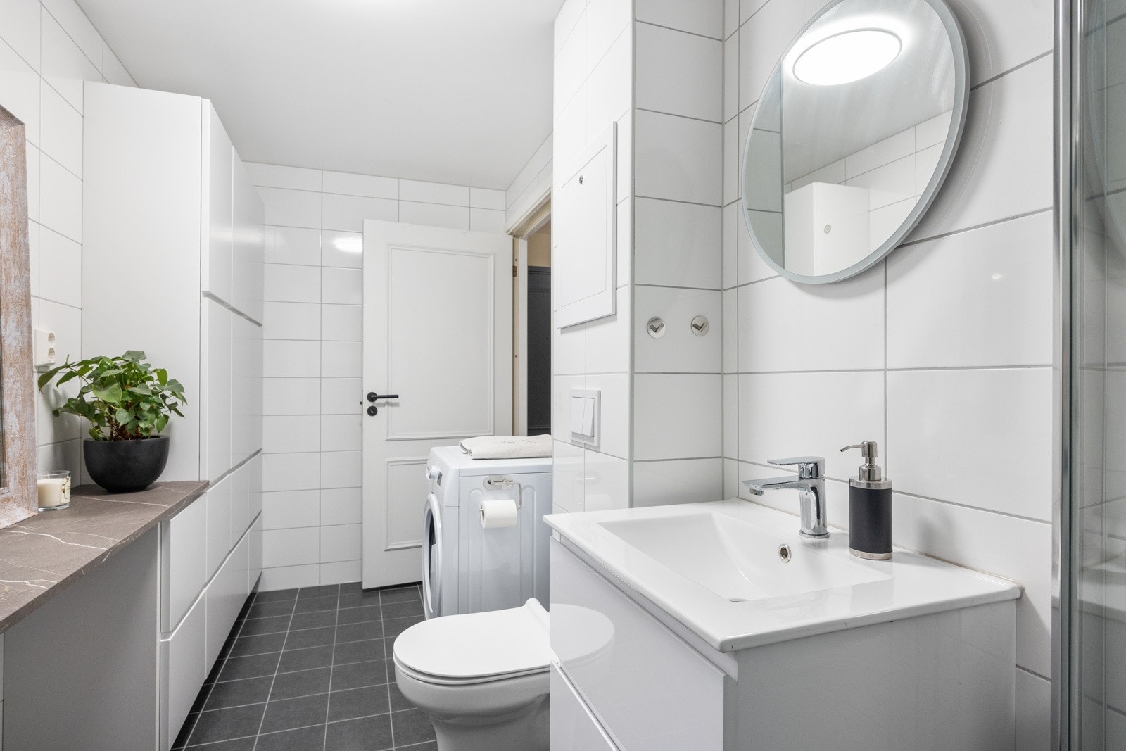 Badet er utstyrt med vegghengt hvit servantinnredning med helstøpt servant, dusjhjørne med svingbare glassdører og vegghengt toalett Galleribilde