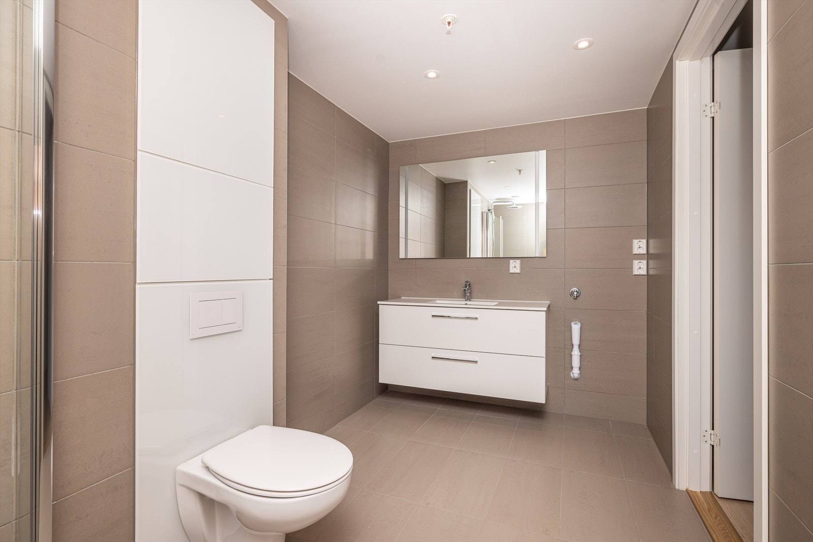 Badet har flislagte gulv og vegger og hvitmalt himling med integrerte led downlights med dimmer. Vegghengt baderomsmøblement med praktiske, dype underskuffer, heldekkende servantplate og stor speilflate over vask med integrert led belysning. Galleribilde