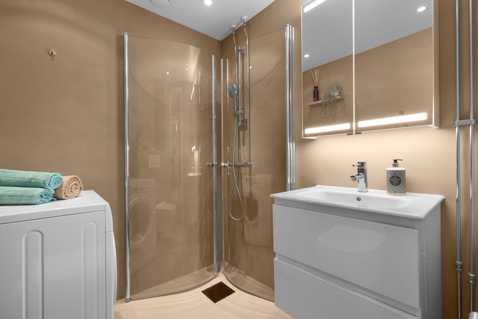 Innredningen består av et dusjhjørne med innfellbare glassdører og dusj direkte på gulv, vegghengt toalett, og et servantskap med belyst speil. Galleribilde