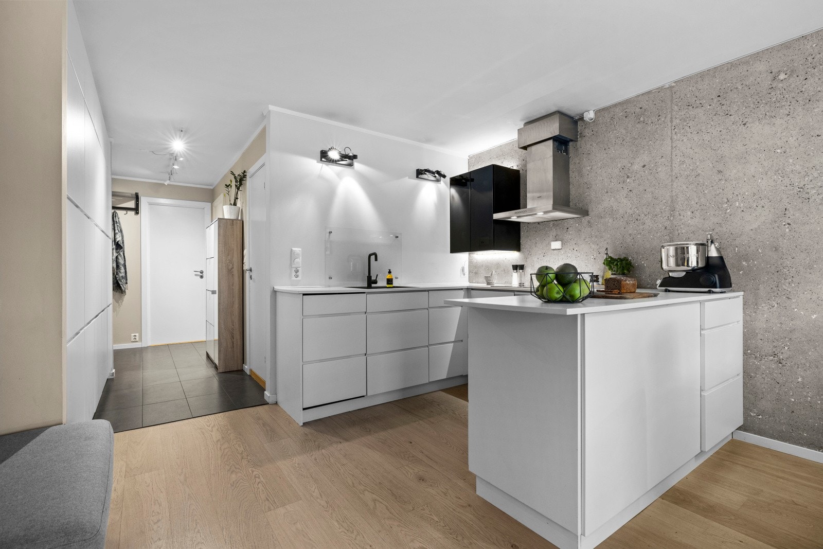 Stilren kjøkkeninnredning fra Kvik med hvite greps frie fronter, backsplashplate ved vask og et overskap med benkebelysning Galleribilde