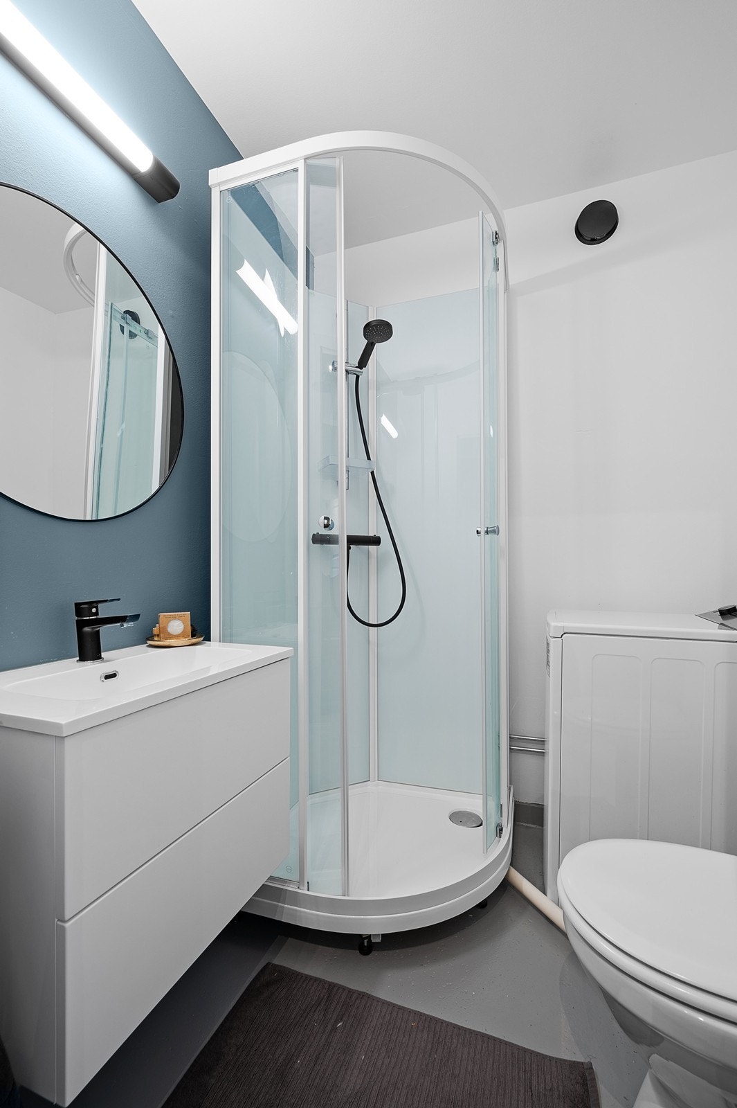 Badet er utstyrt dusjkabinett, hvitt servantskap med to skuffer samt speil på vegg og toalett. Galleribilde