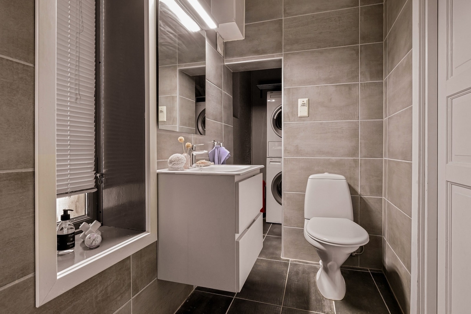 Bad/vaskerom. Gulvet er flisbelagt. Veggene i vaskeromsdelen er malt. Fliser på baderomsdelen på vegger. Galleribilde