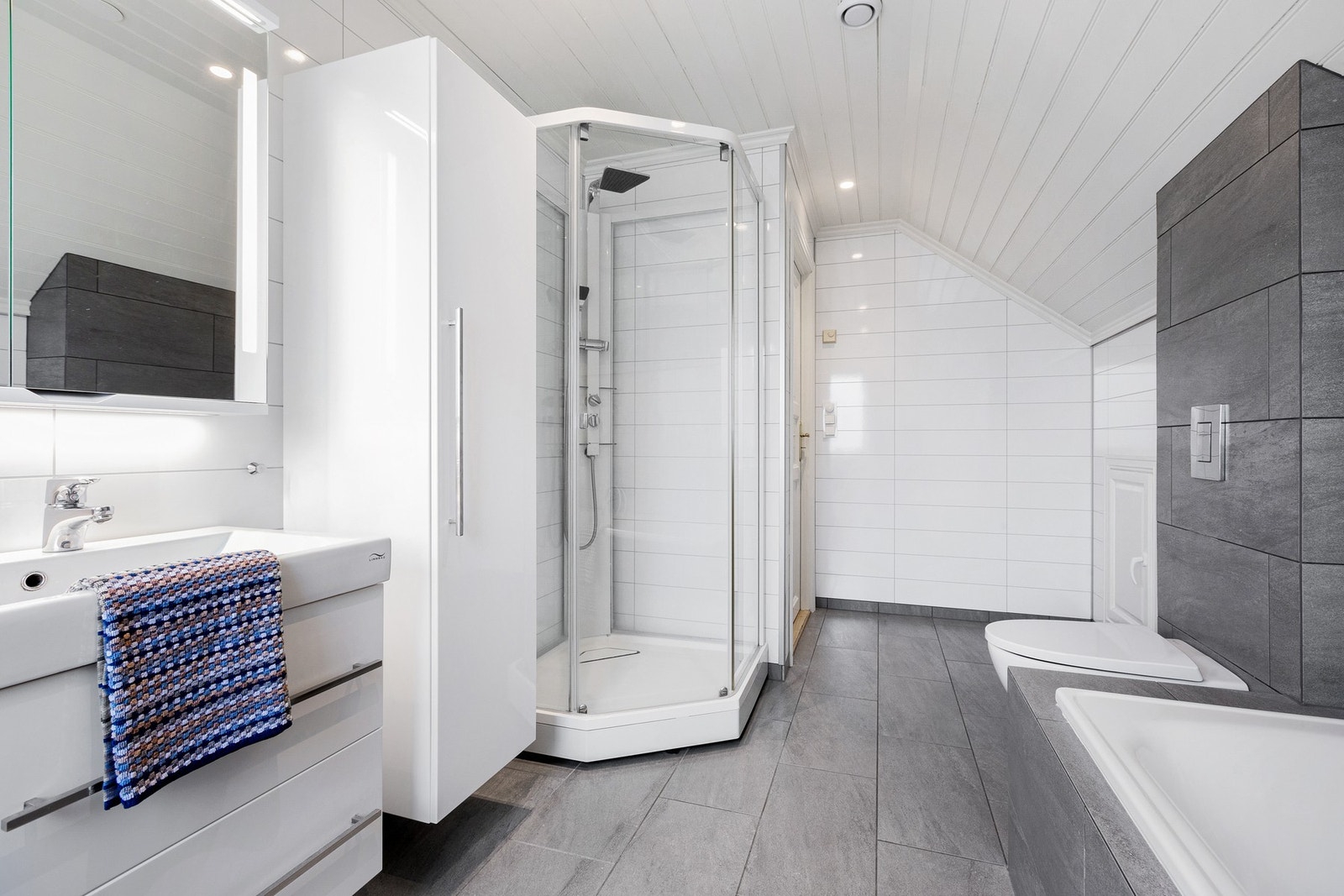 Romslig bad med fliser på gulv og baderomsplater på vegger. Her er det dobbelvask med skapplass, badekar og toalett. Galleribilde