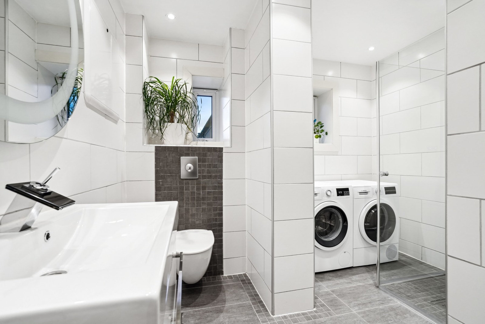 Videre er det en nisje på badet med opplegg for vaskemaskin og et dusjhjørne med glassdører. Galleribilde
