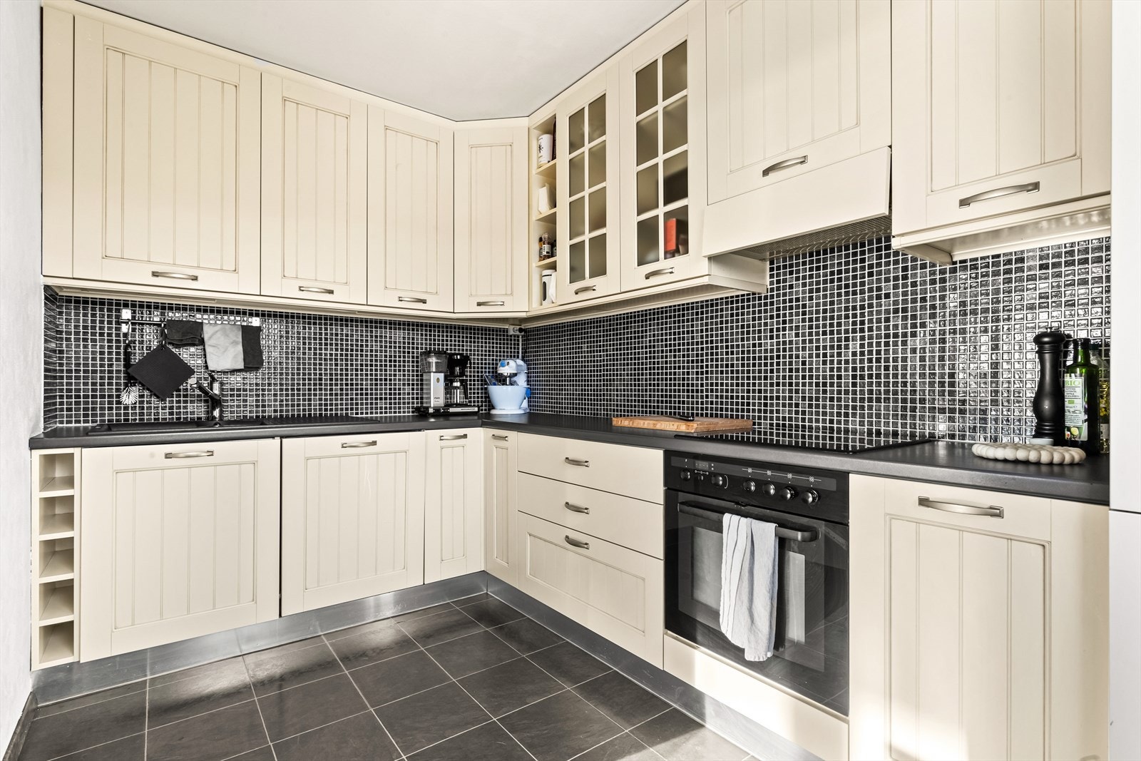 Kjøkkeninnredningen har profilerte fronter med enkelte glassfronter i overskap, samt en benkeplate i laminat med kum i kompositt og tilhørende kjøkkenkran. Galleribilde