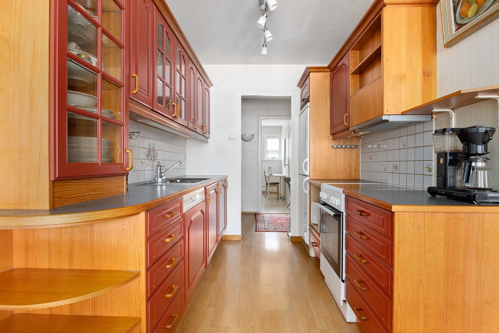 Kjøkken med mye skap- og benkplass. Eldre, men meget velholdt kjøkkeninnredning fra Sigdal med profilerte fronter og fliser over laminert benkeplate. Integrert oppvaskmaskin. Galleribilde