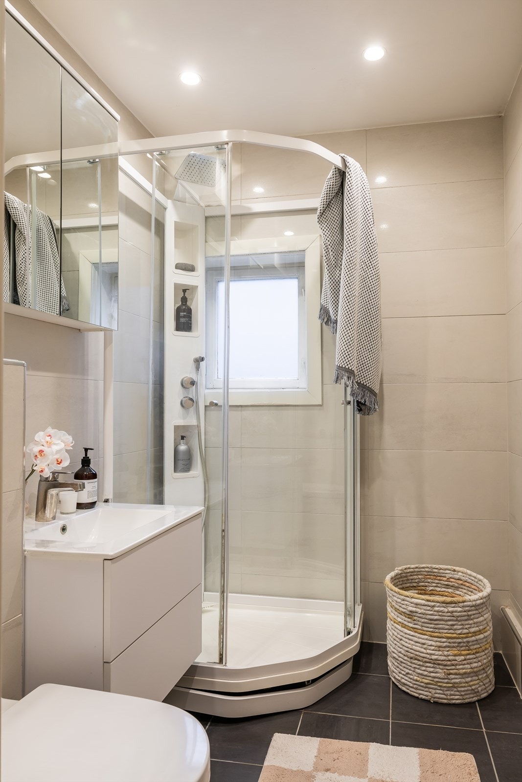 Baderomsinnredning bestående av benkeskap med glatte fronter. Dusjkabinett, servant i helstøpt plate, veggfestet toalett med innebygget sisterne. Galleribilde