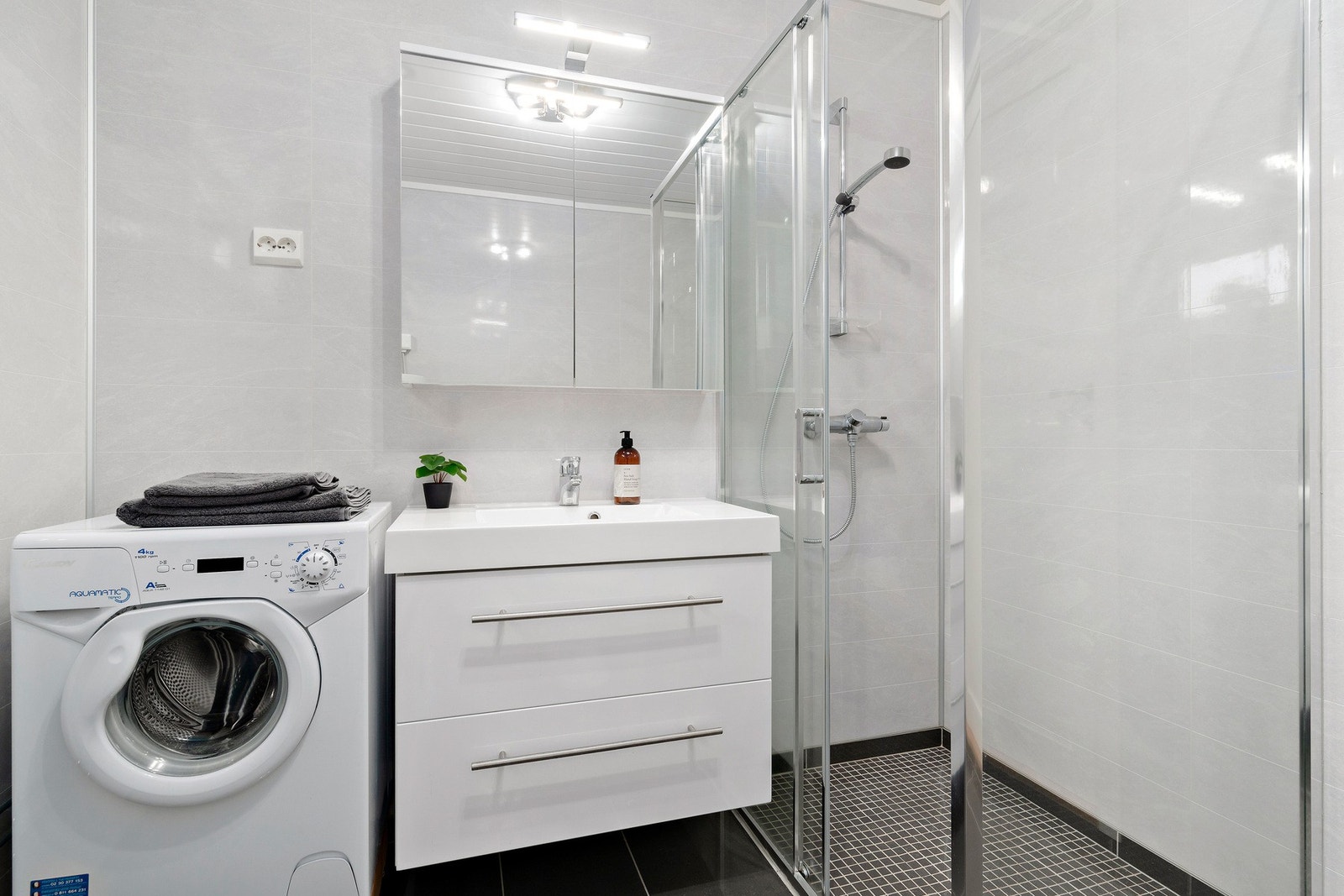 Servantinnredning med helstøpt kompositt servantplate. I tillegg til skuffene er det skap integrert i speilet. Plass for vaskemaskin er viktig. Dusjhjørne med skyvedør. Galleribilde