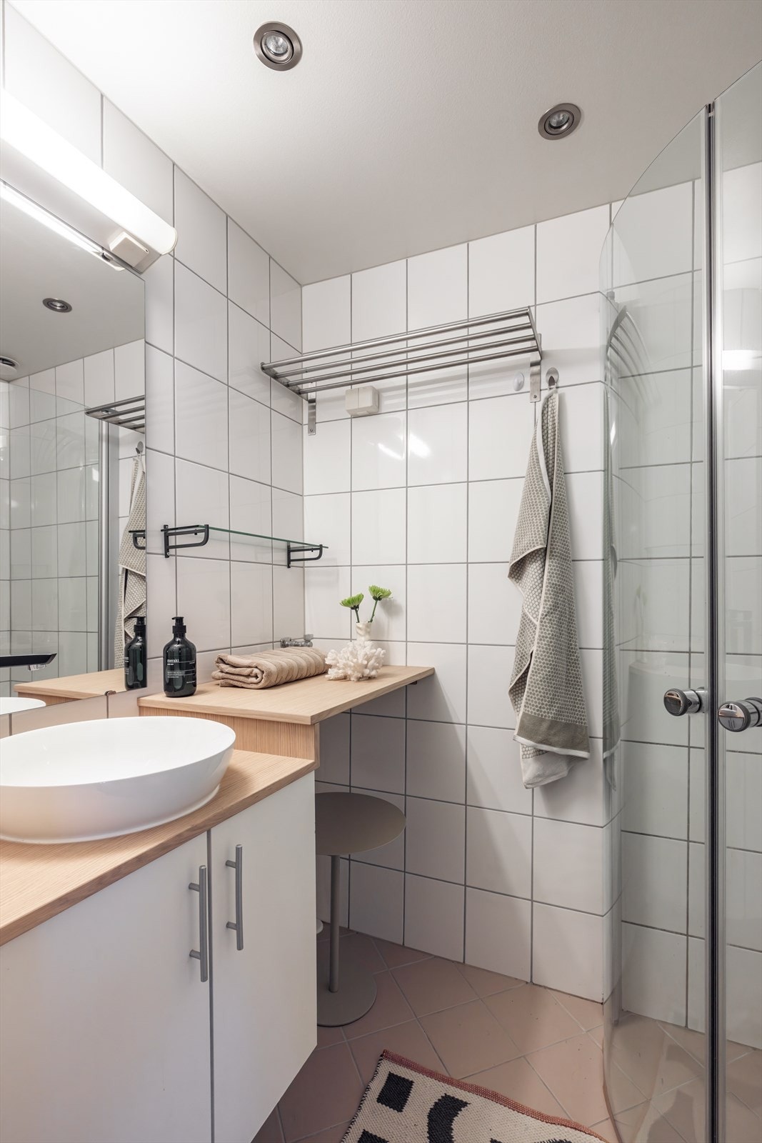 Badet er innredet med en ovenpåliggende servant med praktisk skap under, benkeplate, og vegghengt håndkletørker. Galleribilde