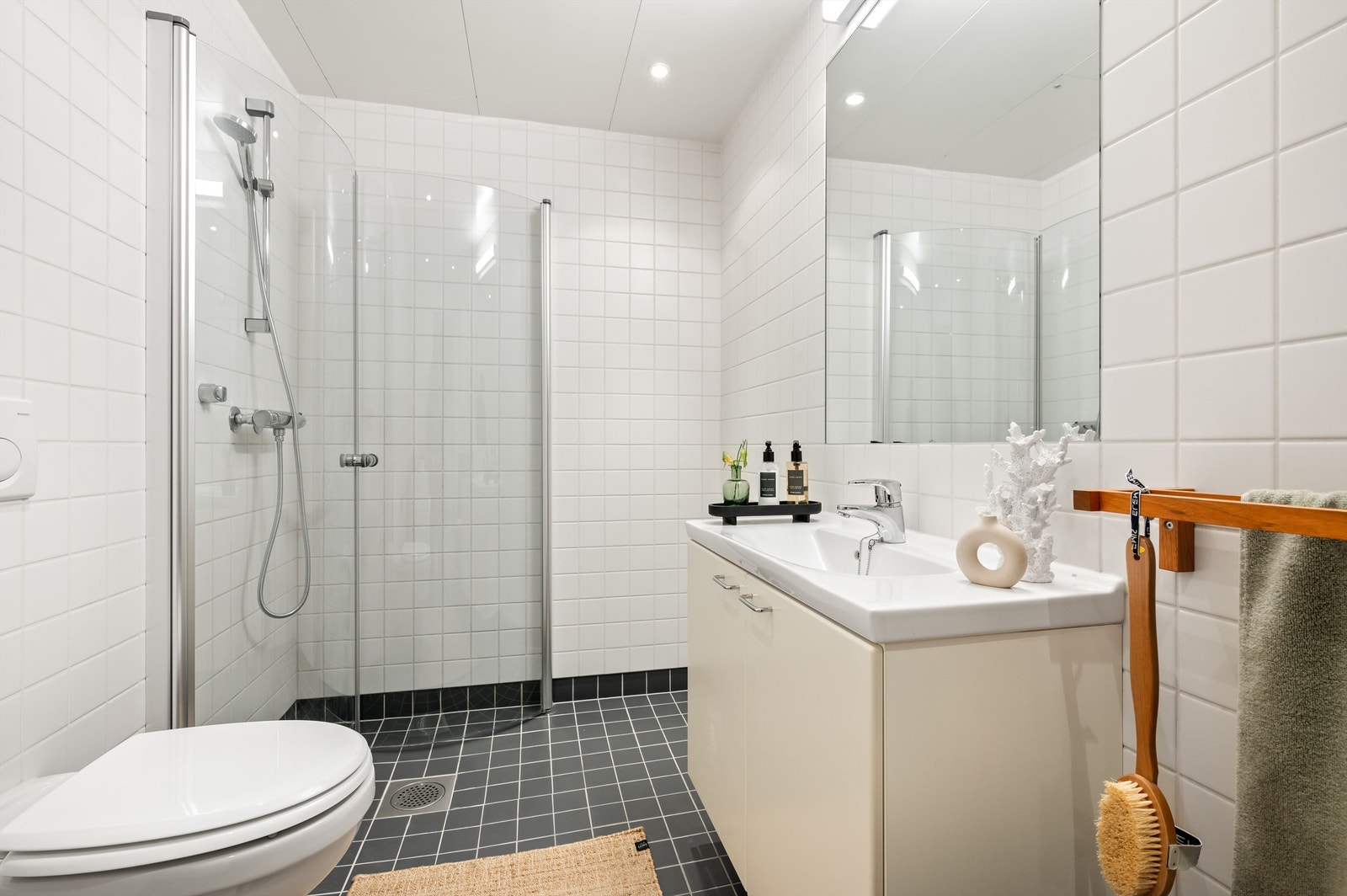 Innredningen består av vegghengt toalett, servant med innredning, innfelt speil over servant med belysning og dusjhjørne med innfellbare glassdører. Galleribilde