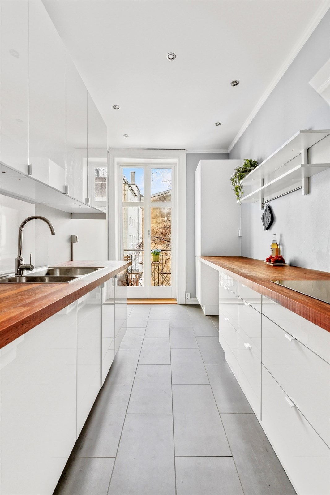 Stilig separat Ikea kjøkken med slette folierte høyglansfronter, heltre benkeplate med sprutplate over koketopp og oppvaskkum, dobbel oppvaskkum og kjøkkenventilator i stål/glass Galleribilde