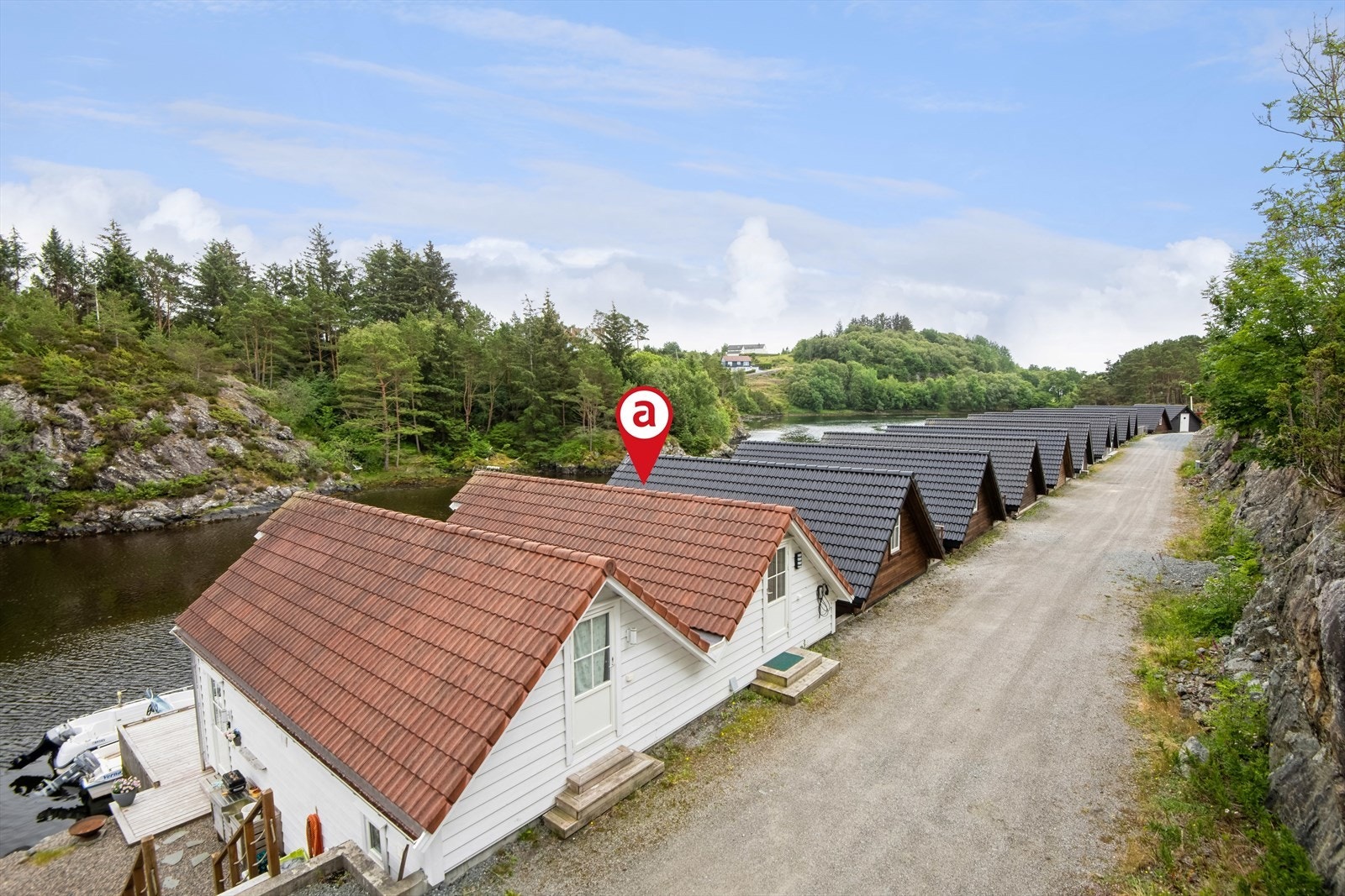 Dronefoto over Mælandsvågen. Det er parkering utenfor naustet og innstalert elbillader. Galleribilde