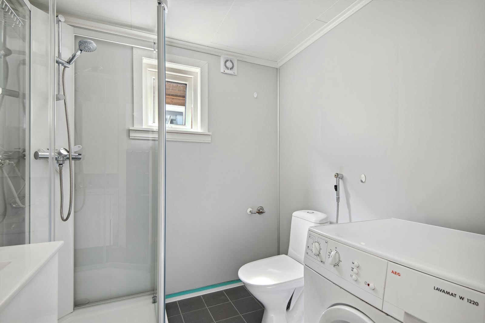 Badet er innreia med golvståande toalett, dusjkabinett, benkeskap med vask, speil, varmekablar i golv og vaskemaskin. Galleribilde