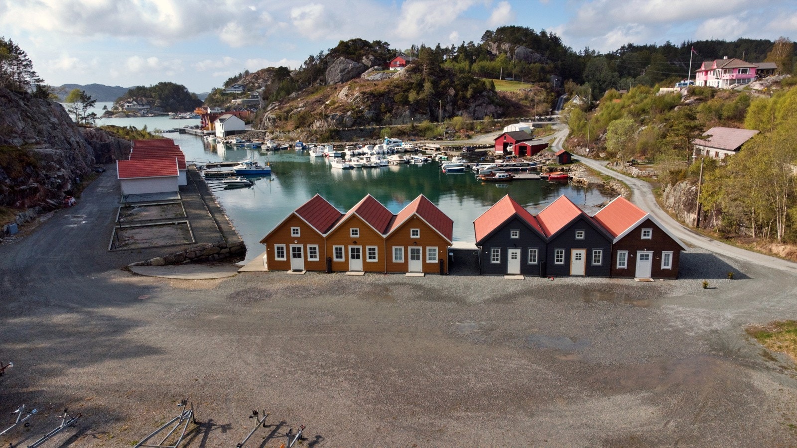 Oversiktsbilete over naustområdet. Felles parkeringsplass er stor, og fleire har båthengjarane sine ståande her. Galleribilde