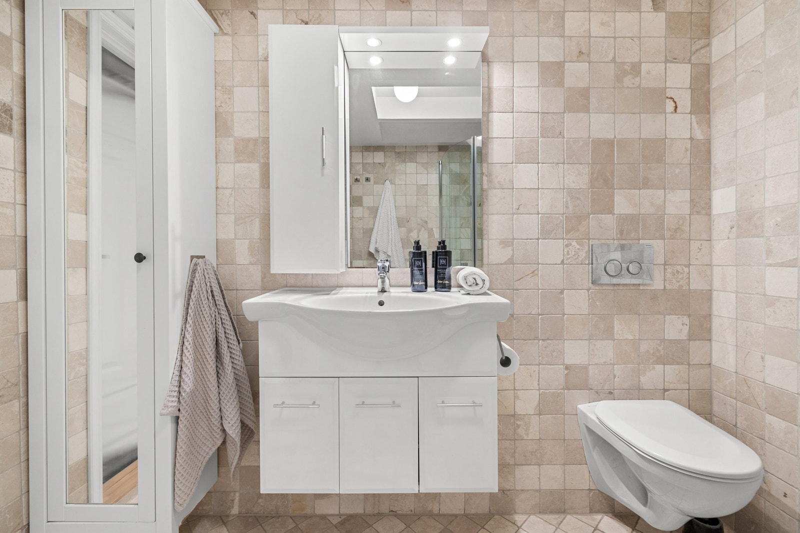 Det er vegghengt skap med ovenpåliggende servant, samt skap på vegg med speil og belysning. Vegghengt toalett. Galleribilde