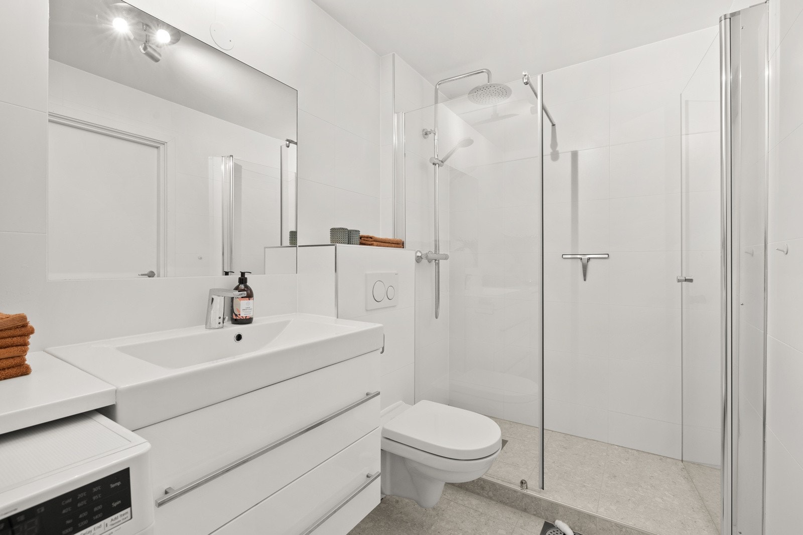 Baderommet er utstyrt med flislagte overflater, dusjsone med regnfallsdusj, opplegg for vaskemaskin og vegghengt wc Galleribilde