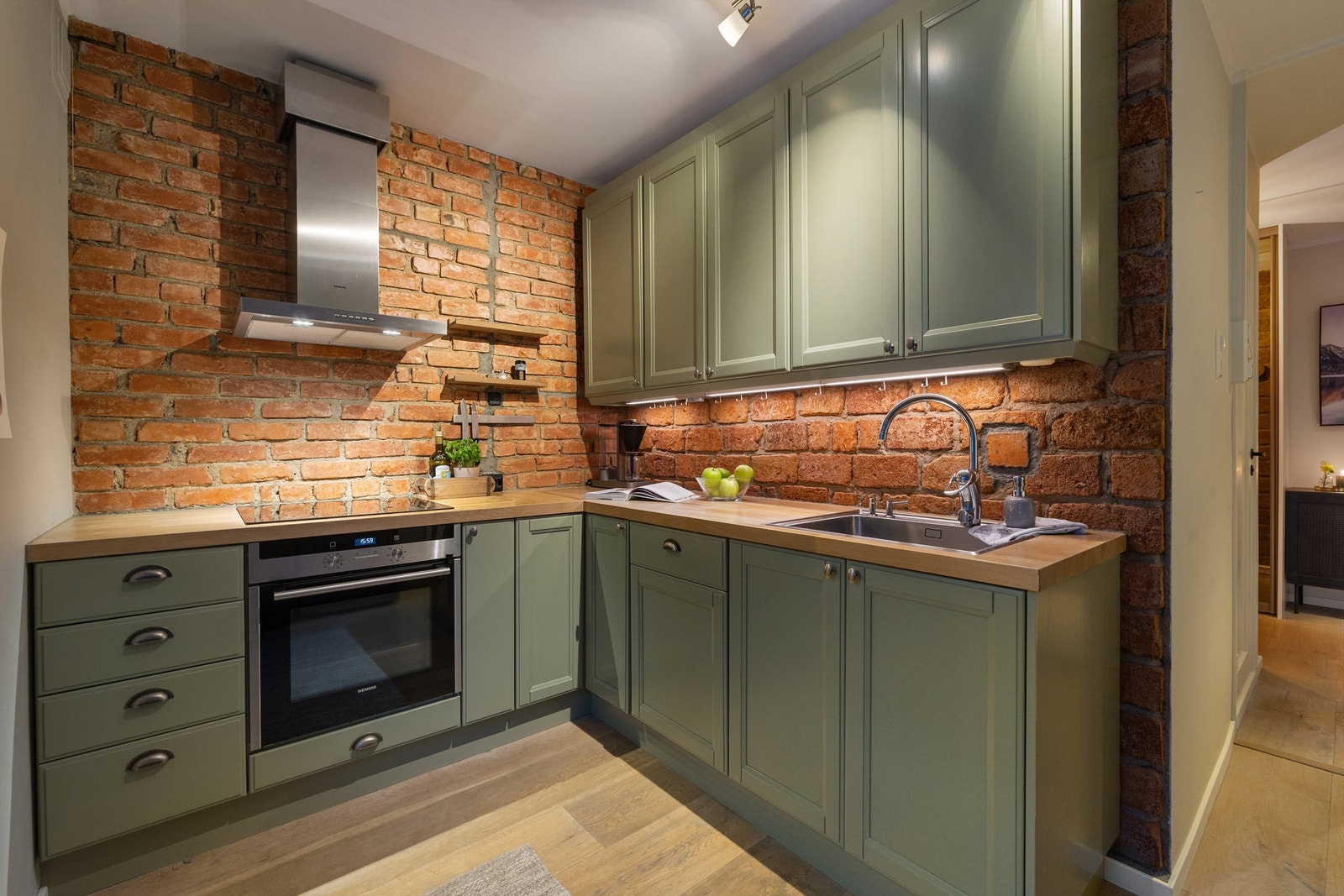 Kjøkkenet har nedfelt oppvaskkum i rustfritt stål med ett-greps armatur (2021). Benkeskapsbelysning med stikkontakter over kjøkkenbenk. Kjøleskap, fryser, oppvaskmaskin (2021), stekeovn og induksjonstopp (2022). Vegghengt ventilator med kullfilter. Galleribilde