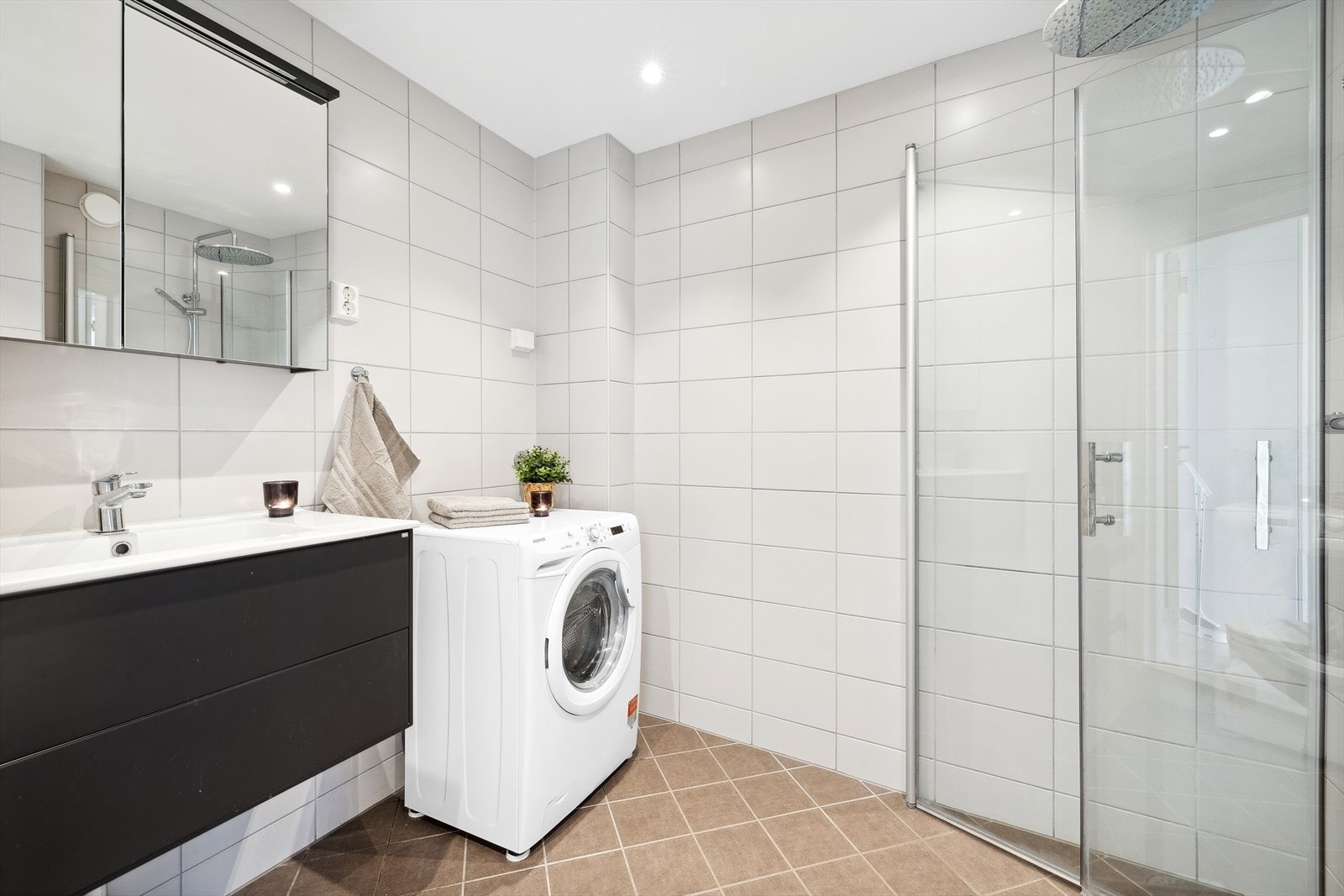 Badet har moderne baderomsinnredning med lagringsplass, uttak til vaskemaskin, toalett og dusjhjørne med innfellbare vegger Galleribilde