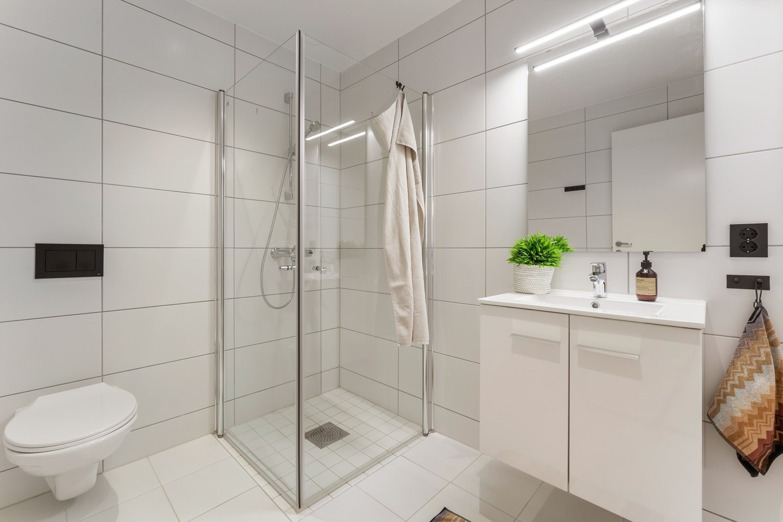 Badet er helfliset med lyse og stilrene fliser med termostatstyrte varmekabler i gulv Galleribilde