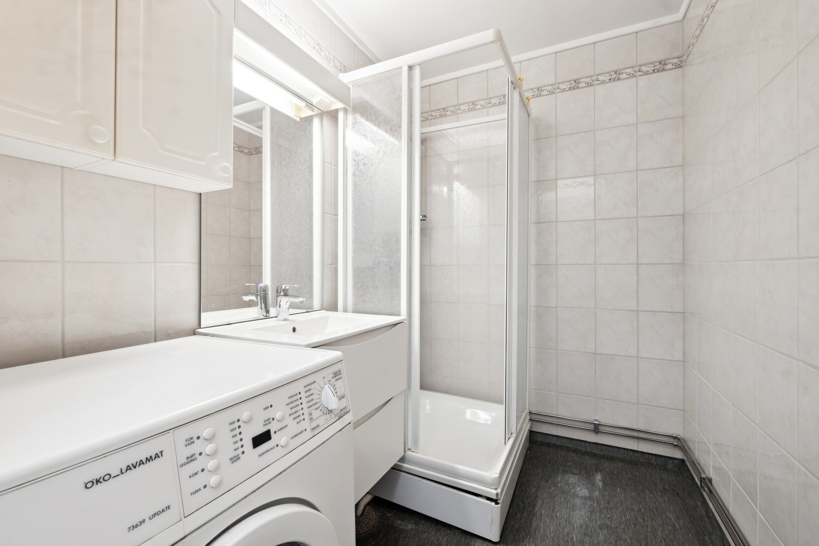 Bad med flislagte vegger vurdert til å være fra byggeår. Badet ble flislagt på 90-tallet. Badet inneholder vegghengt servantskap med ovenpåliggende servant og ett-greps armatur, speil, belysning, stikkontakt og overskap over servant. Galleribilde