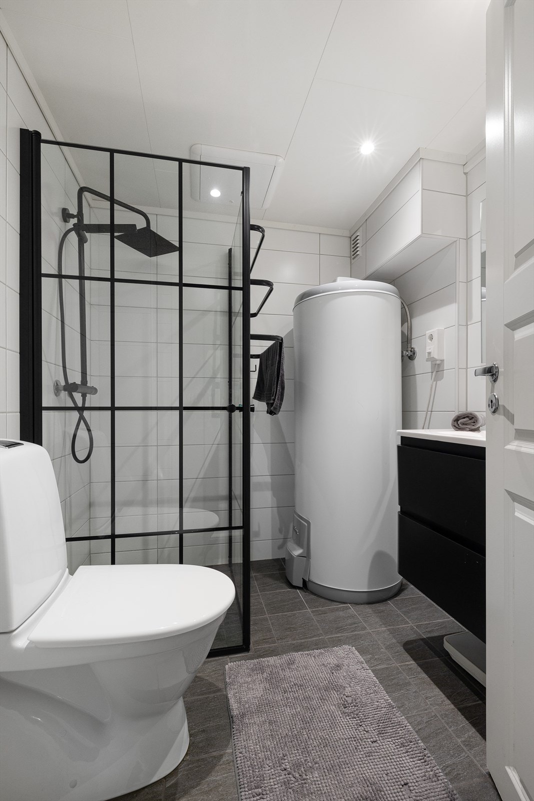 Badet er helfliset og utstyrt med dusjhjørne med takdusj, toalett, servantmøbler, speil med integrert belysning og varmtvannsbereder. Galleribilde