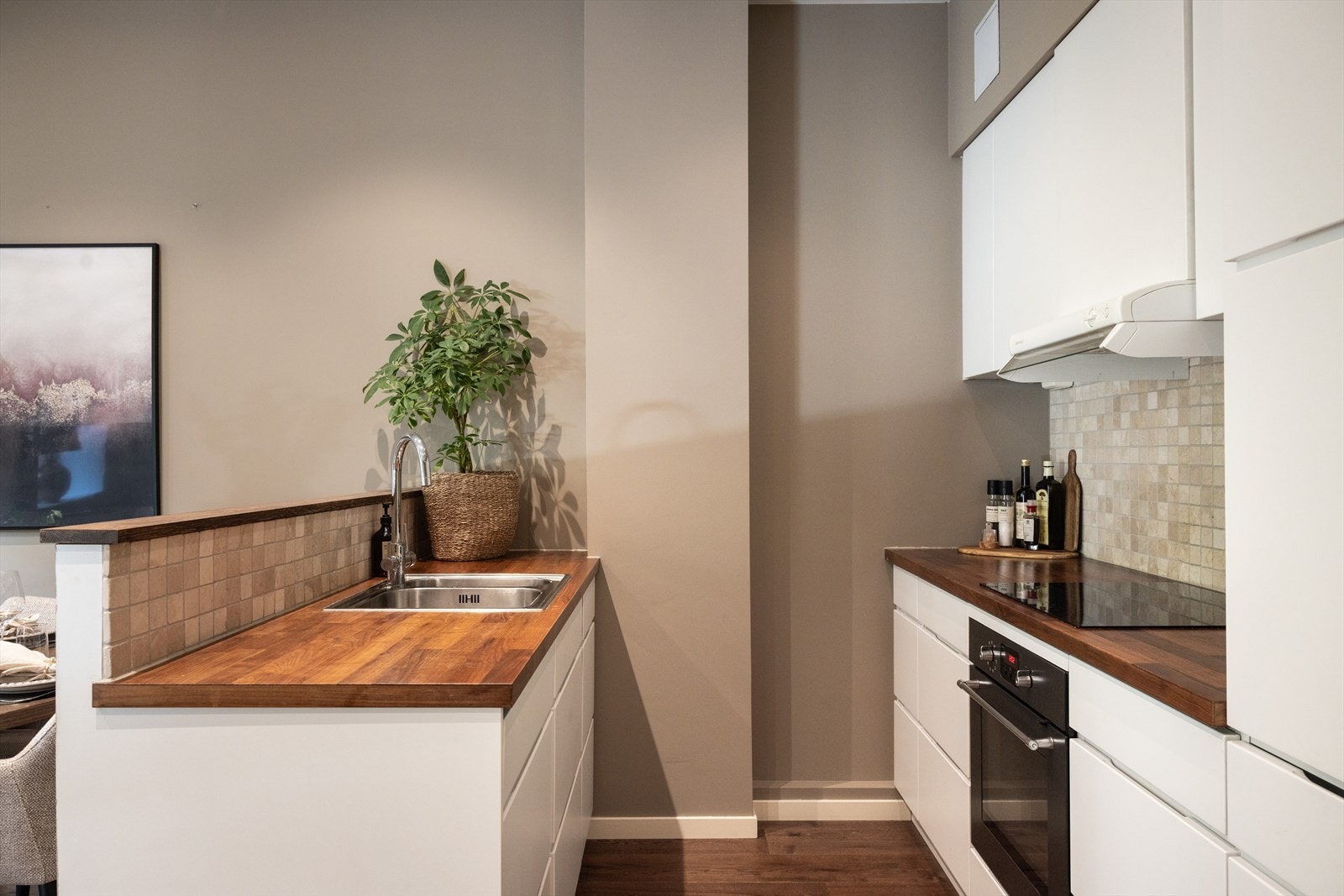 - KVIK-kjøkken fra 2015. Moderne kjøkkeninnredning med glatte fronter, heltre benkeplate med nedfelt vask-og skyllekum, samt fliser og belysning over benkeplaten - Galleribilde