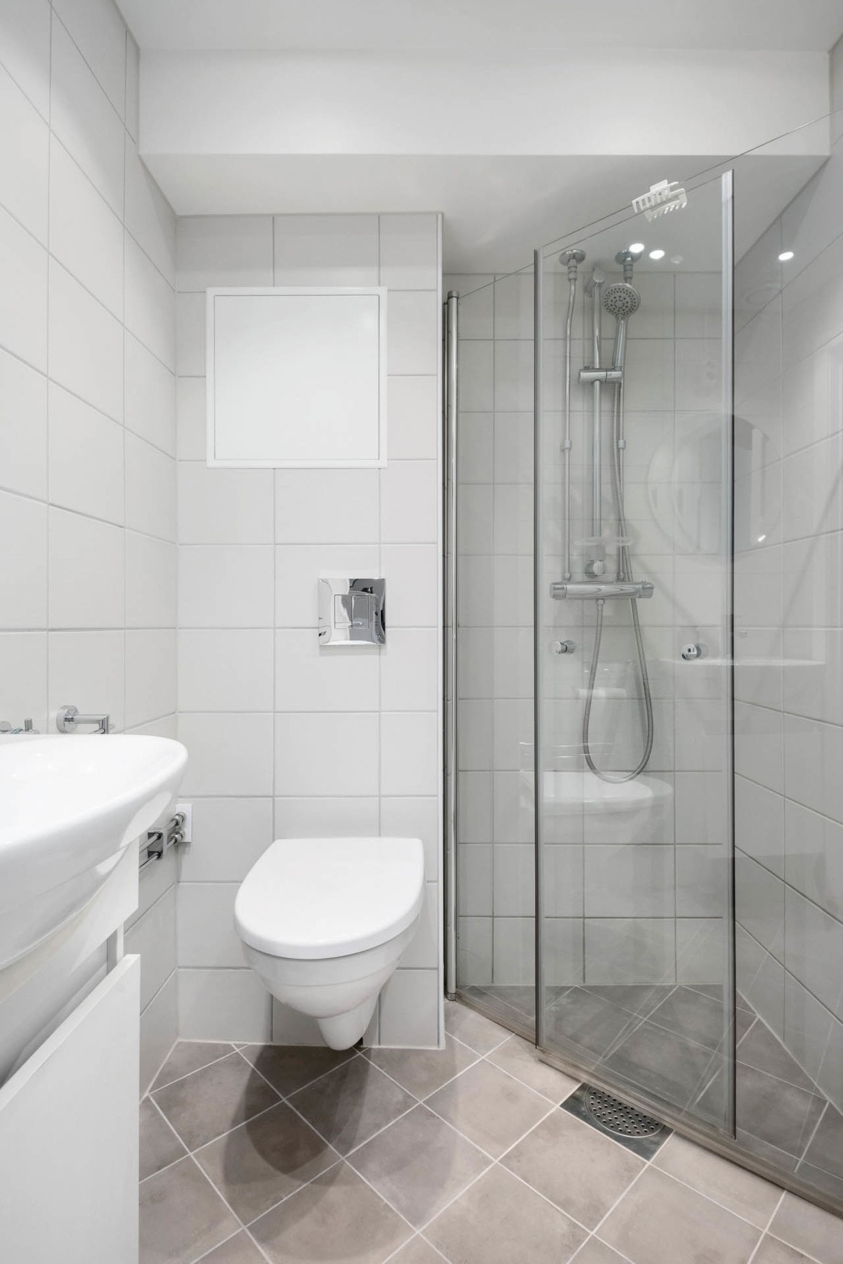Badet inneholder vegghengt servantskap med ovenpåliggende servant og ett-greps armatur, speil og stikkontakt over servant, vegghengt toalett og dusjhjørne med innfellbare glassdører. Galleribilde
