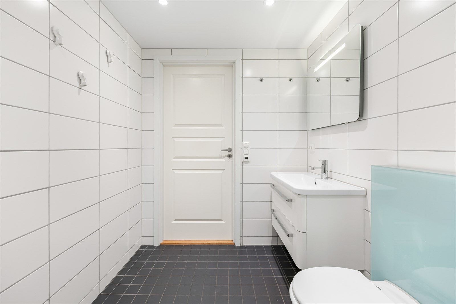 Badet er utstyrt med dusjnisje med innfellbare dører, servant med underskap og speil, vegghengt toalett samt opplegg for vaskemaskin. Galleribilde