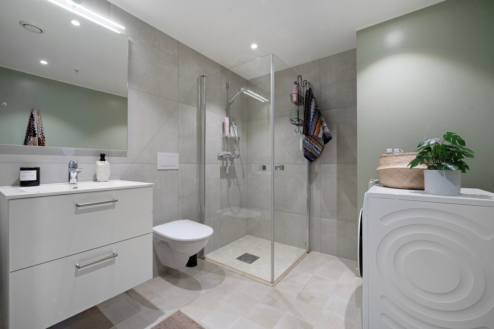 Meget innbydende og flott bad målt til 5,1 kvm. Badet er innredet med innfellbare og plassbesparende dusjvegger i glass, veggmontert WC, kran/avløp for vaskemaskin samt servant på underskap og speil. Galleribilde