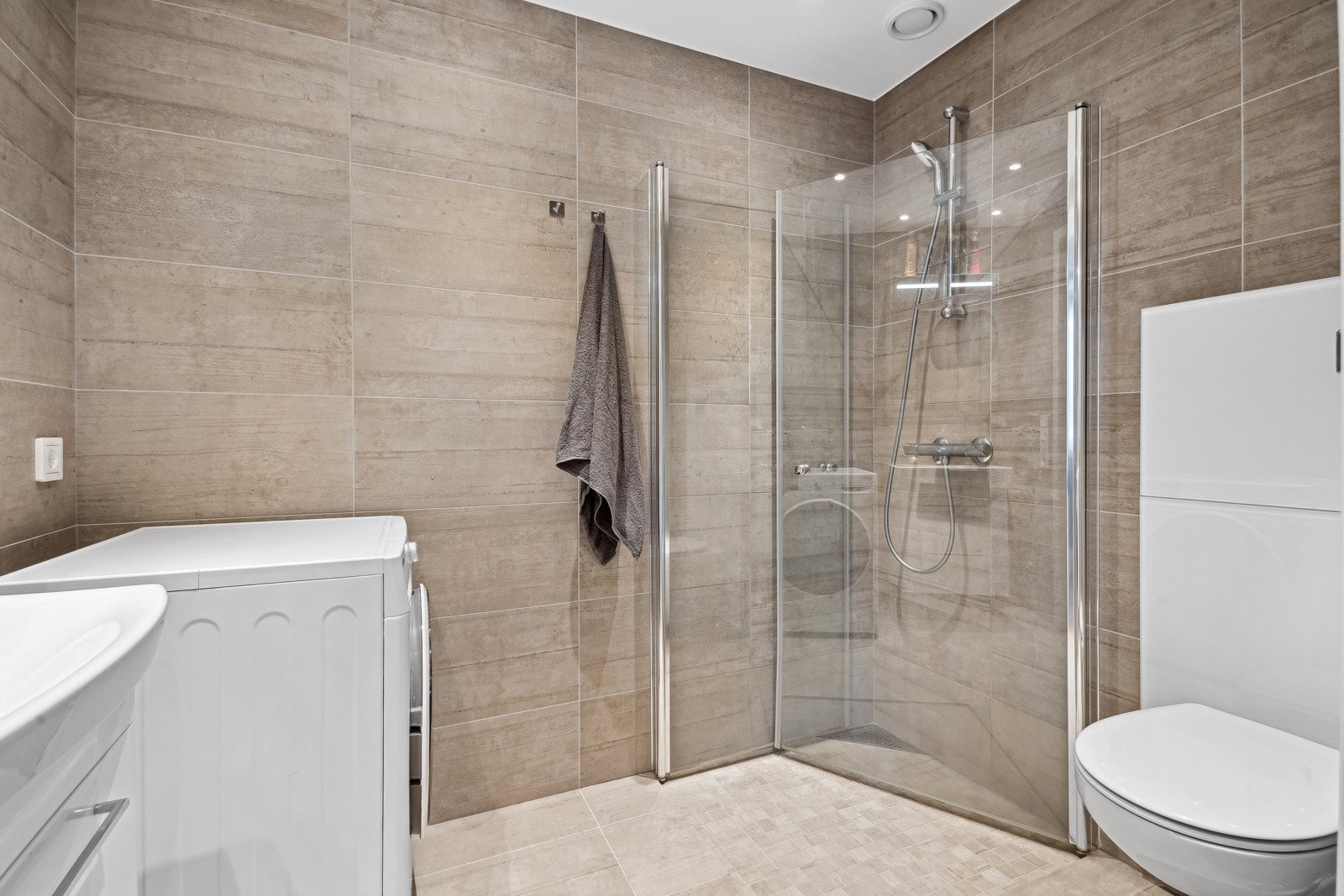 Badet er utstyrt med dusjhjørne, innfellbare glassdører, mekanisk avtrekk, vegghengt toalett, rørfordelingsskap og opplegg for vaskemaskin. Galleribilde