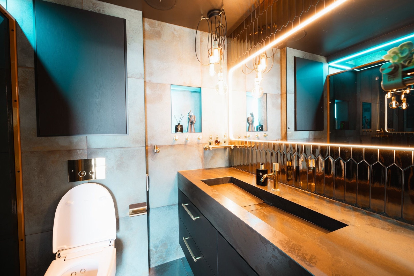 Hovedbadet byr på eksklusive detaljer – Geberit spyletoalett med fjernkontroll, helstøpt servantbenk i stein og gulltonede fliser bak speilet som gir rommet et luksuriøst preg Galleribilde