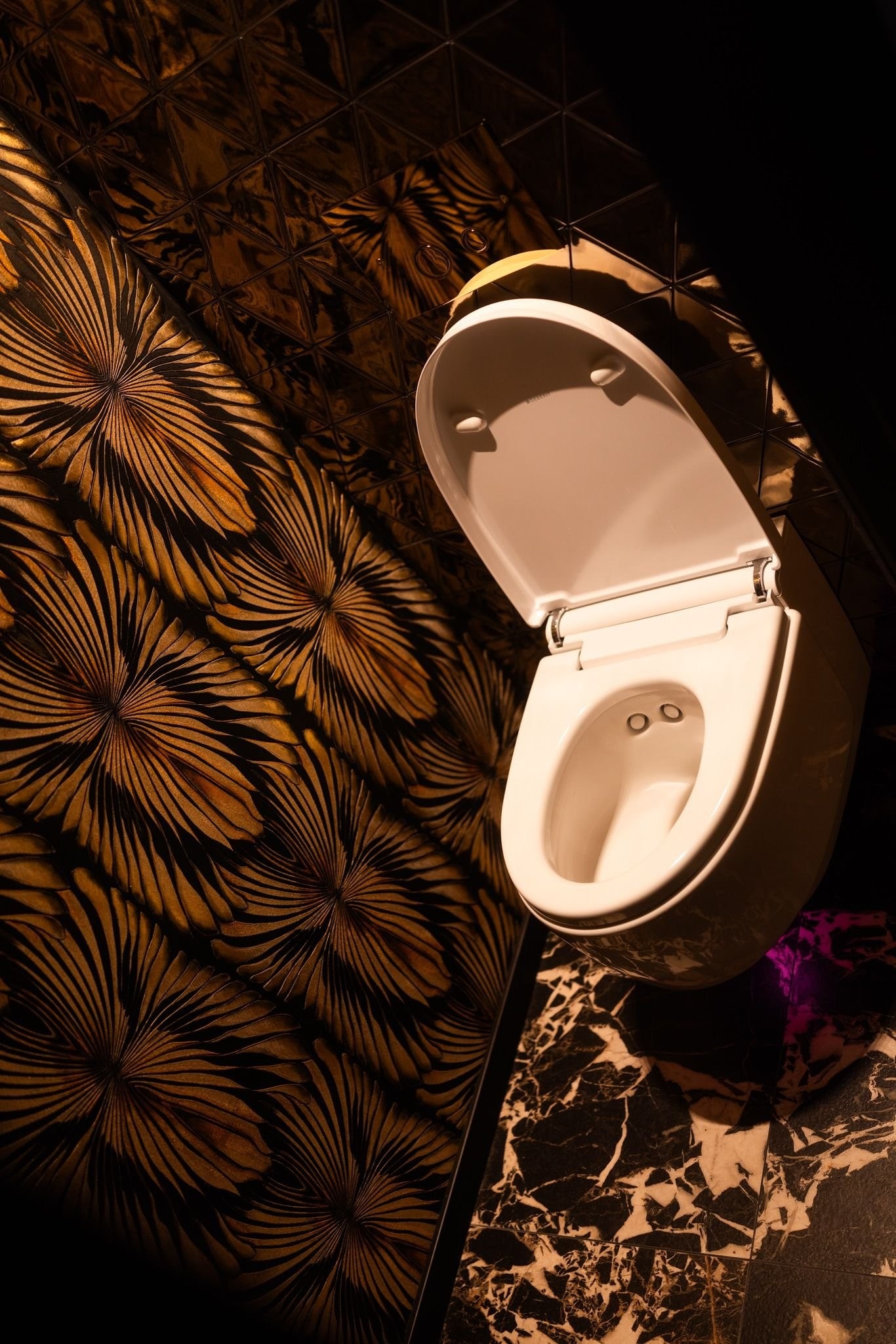 Gjestetoalettet er utstyrt med Geberit spyletoalett med fjernkontroll. Bakveggen er kledd i gulltonede fliser som tilfører rommet en glød og et markant preg av eleganse Galleribilde