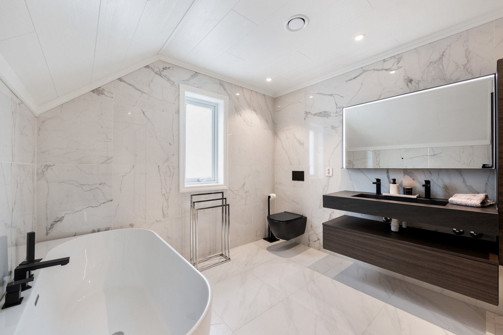 Badet har helfliser overflater, varmekabler, balansert ventilasjon og både badekar og stor dusjnisje. Galleribilde