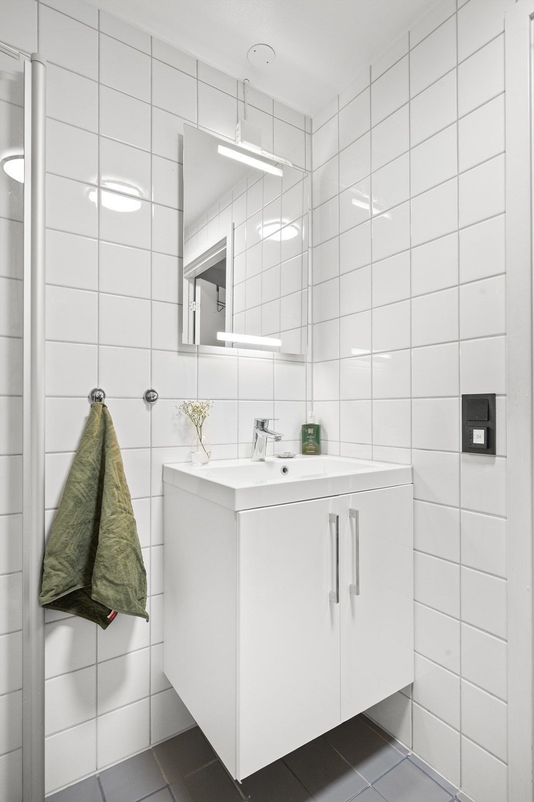 Badet er innredet med vegghengt toalett, dusjhjørne med svingbare glassdører og baderomsinnredning med skap, nedfelt servant og speil med belysning. Galleribilde