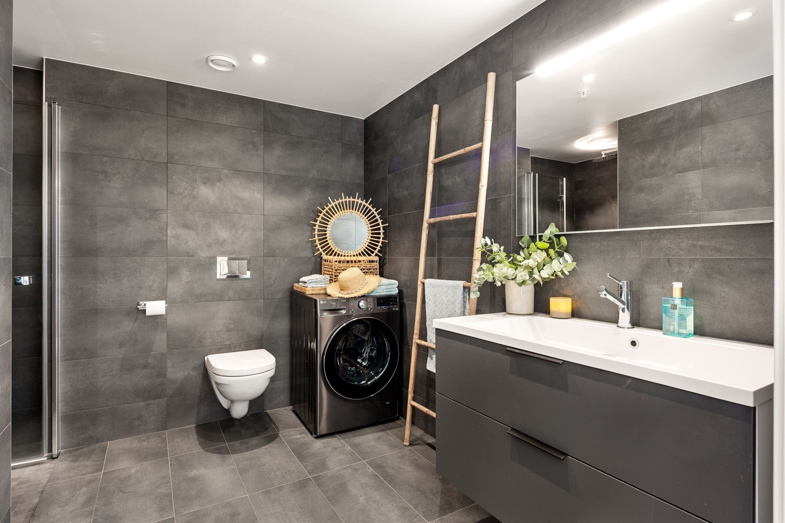 Moderne bad med vegghengt toalett, dusjhjørne, vaskemaskin og stor servant med speil. Galleribilde